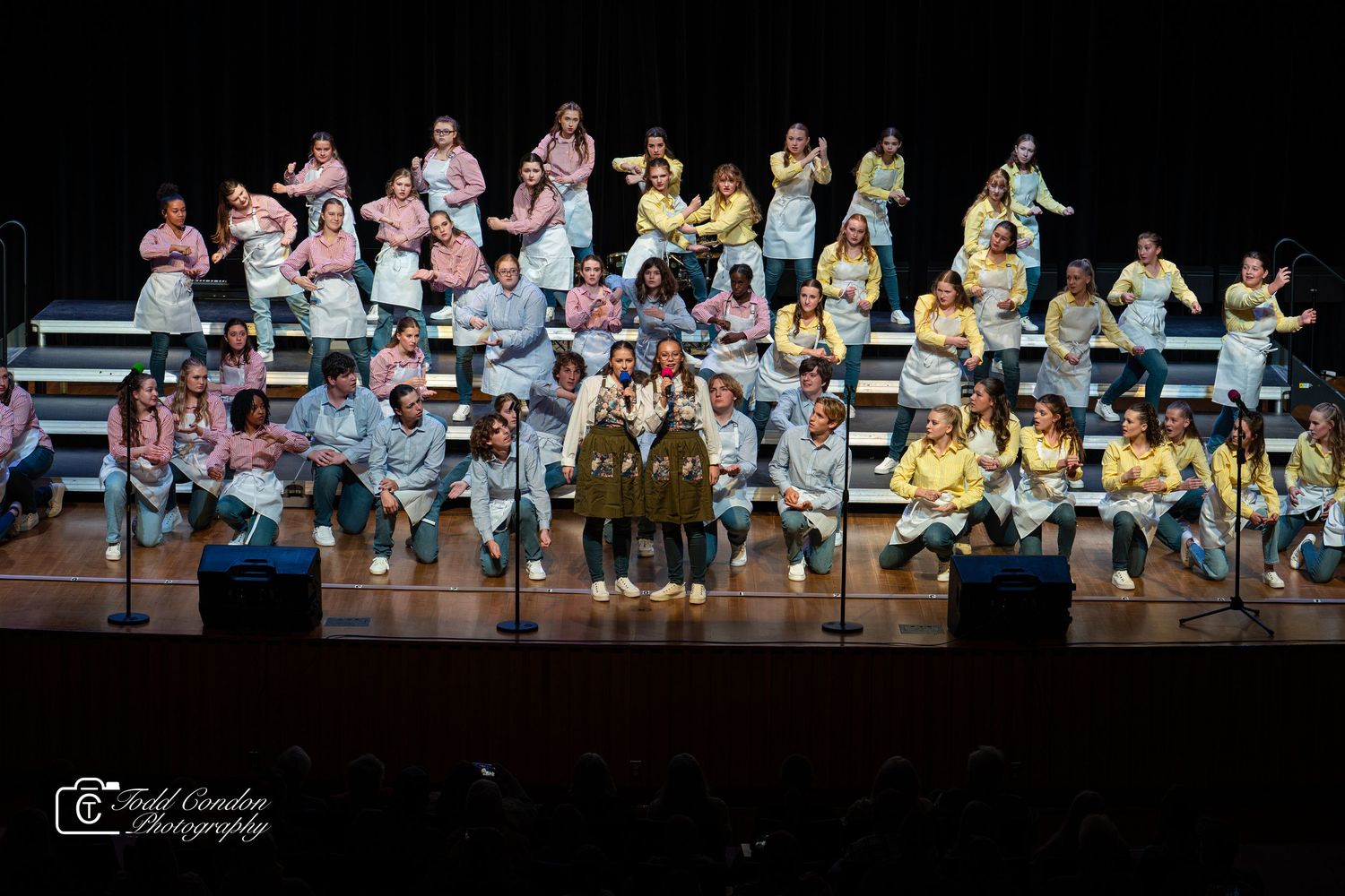 Performance group in colorful outfits arranged on stage during a theatrical production.