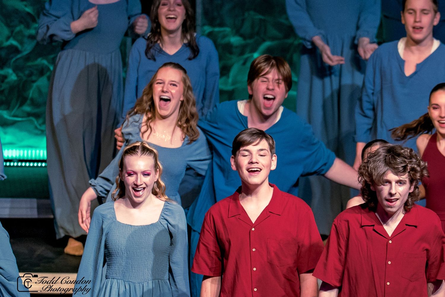 Performers in blue and red costumes singing together energetically during a stage performance.