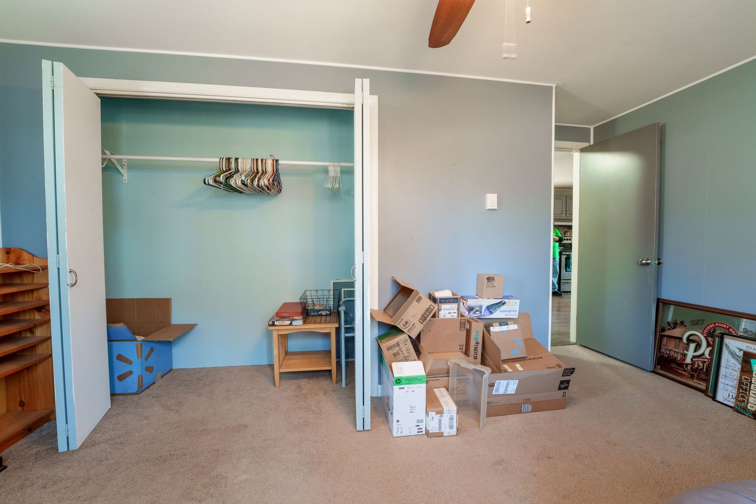 Panoramic view of an empty room with light blue walls, ceiling fan, and scattered moving boxes.