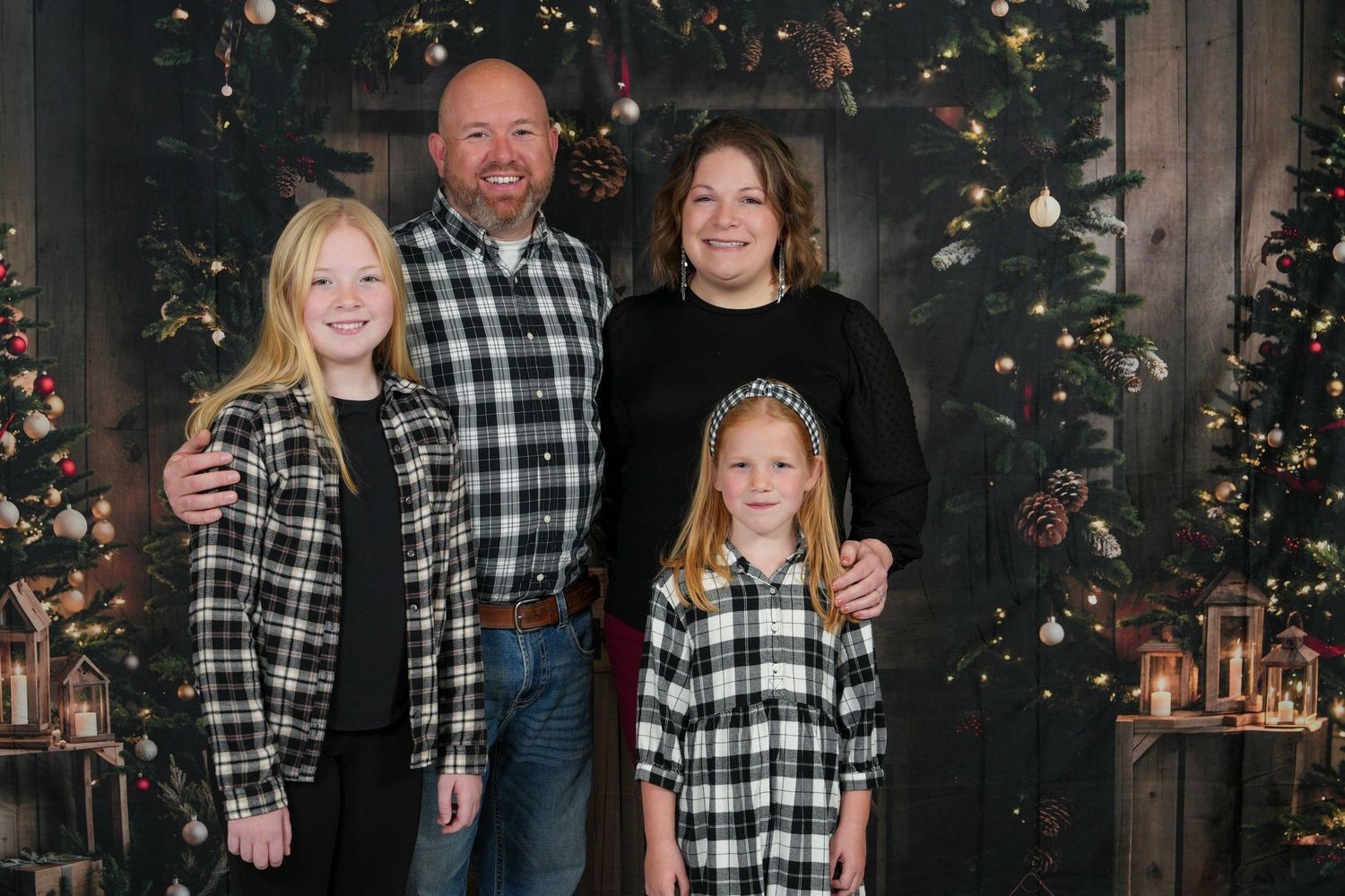 Family wearing coordinated black and white buffalo plaid outfits poses in front of decorated Christmas tree.