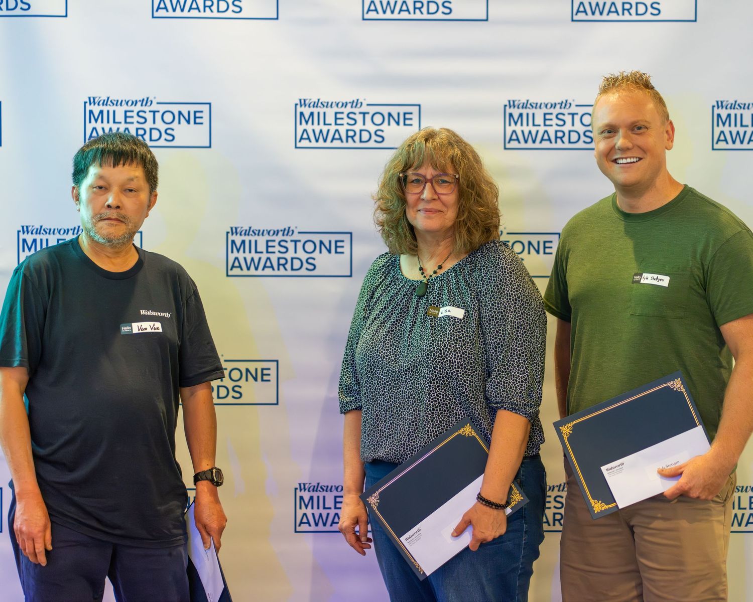 A group of people standing in front of a blue and white Milestone Awards backdrop holding certificates.