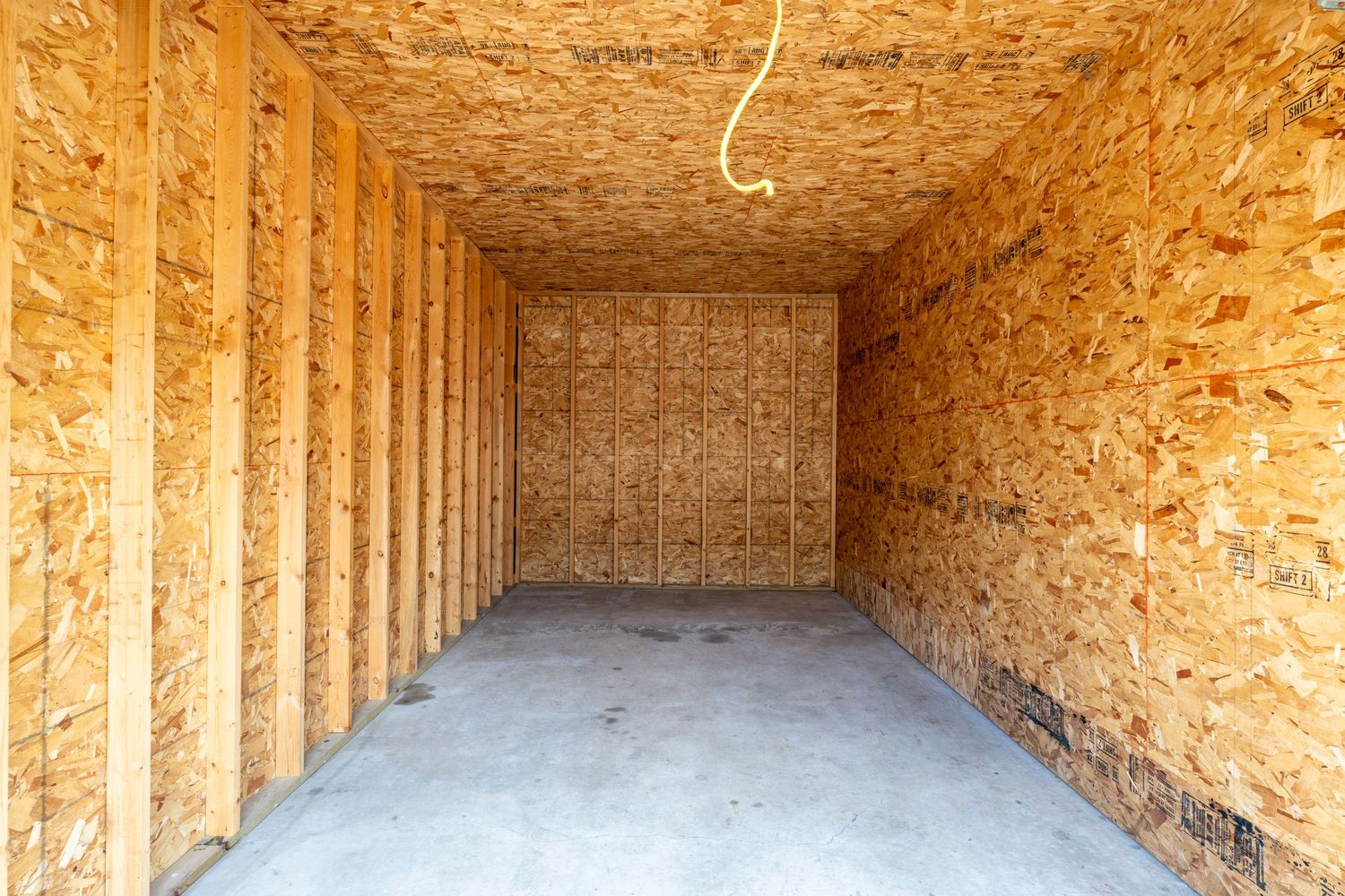 Long wooden hallway under construction with exposed OSB panels and framing studs illuminated by natural light.
