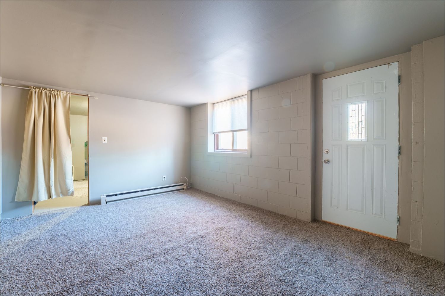 Empty room interior with beige walls, carpeted floor, and natural light coming through windows.