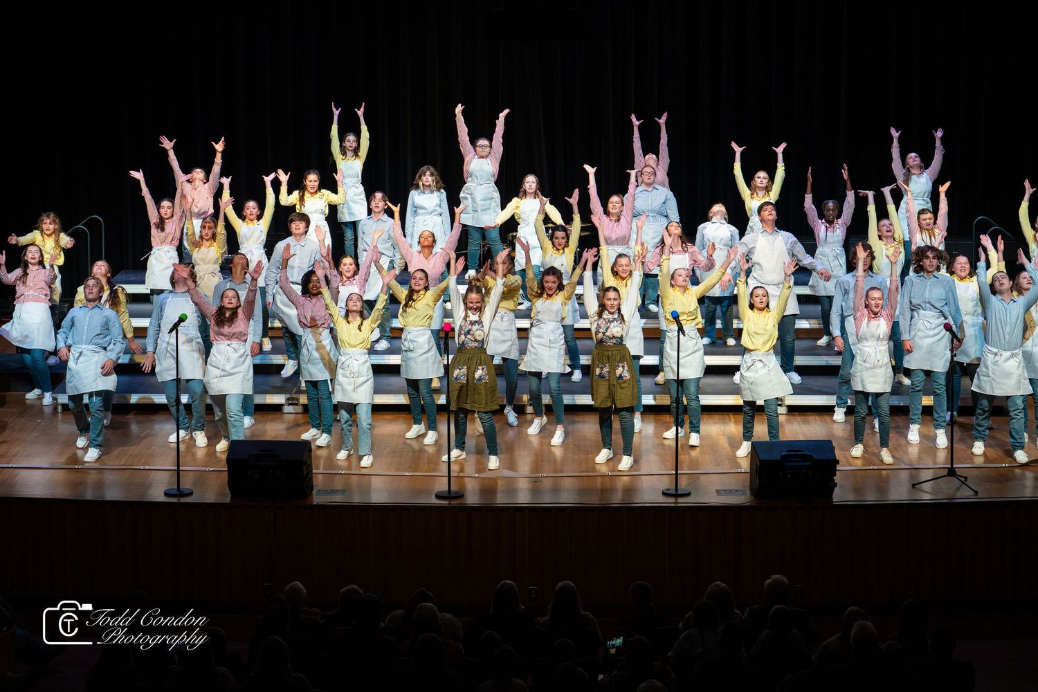 Dancers on stage perform with raised arms in coordinated formation during theatrical performance.