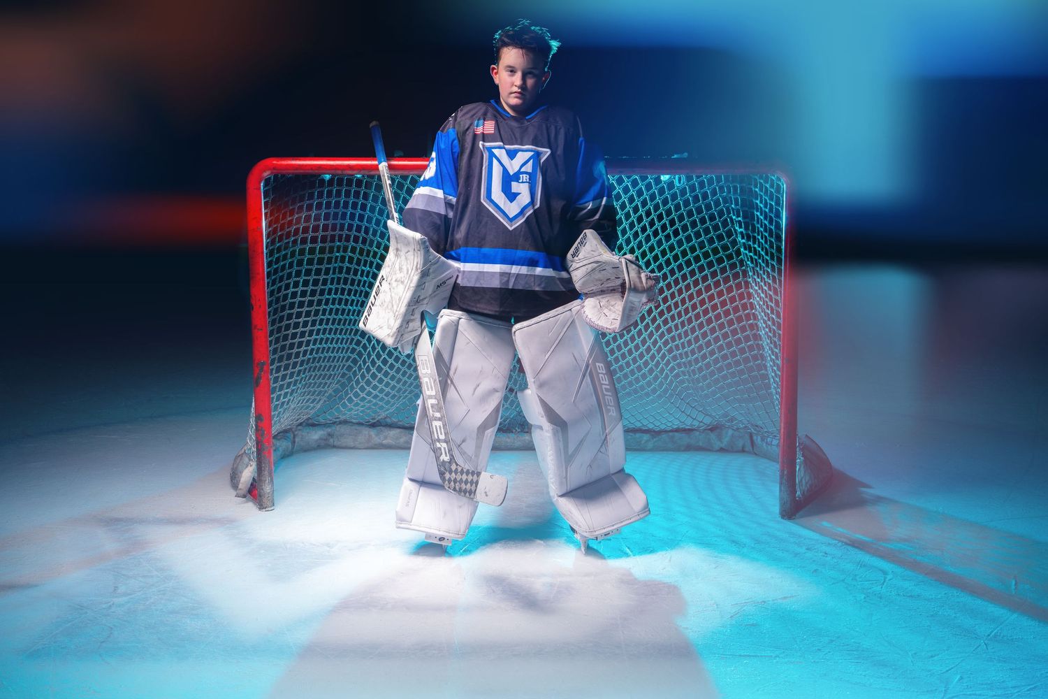 A hockey goalie stands in the crease with blue lighting effects creating a dramatic atmosphere on the ice.