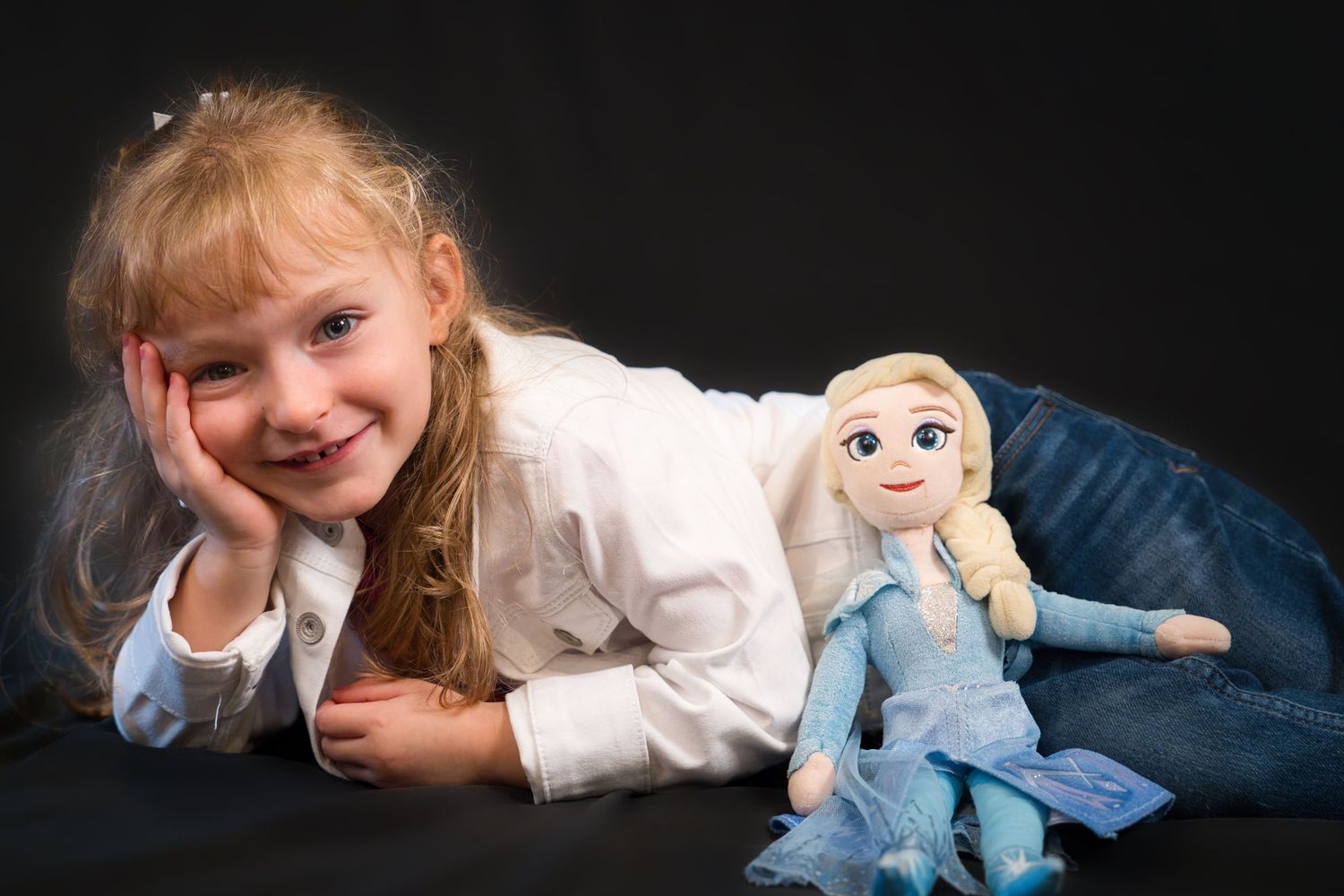 A young child lying on a dark background with a plush Elsa doll from Disney's Frozen movie.
