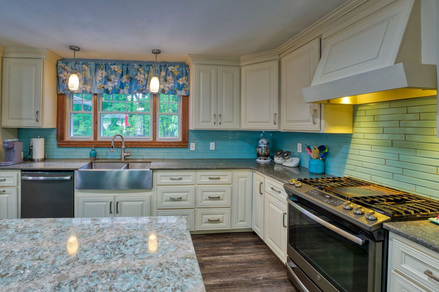 White kitchen with granite countertops, teal subway tile backsplash, stainless steel appliances, and pendant lights over farmhouse sink.
