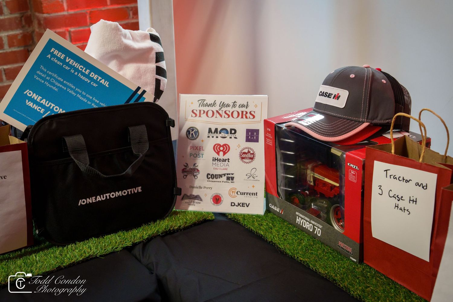 Sponsor thank you display with branded hat, tote bag, and gift items on artificial grass at an automotive event.