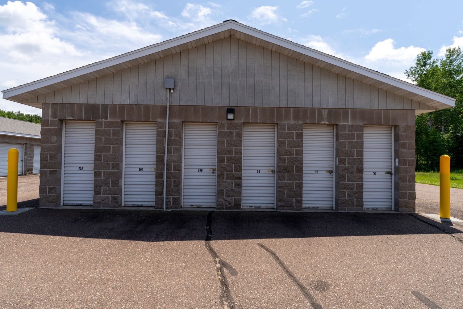 A long row of beige storage units with white garage doors under a blue sky with white clouds.