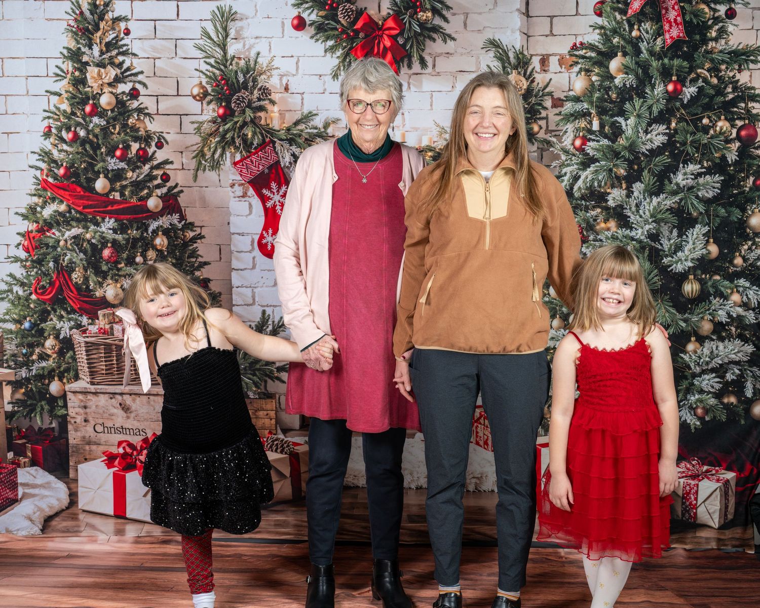 A festive holiday photo session with a white brick backdrop, decorated Christmas trees, and red and green decor.