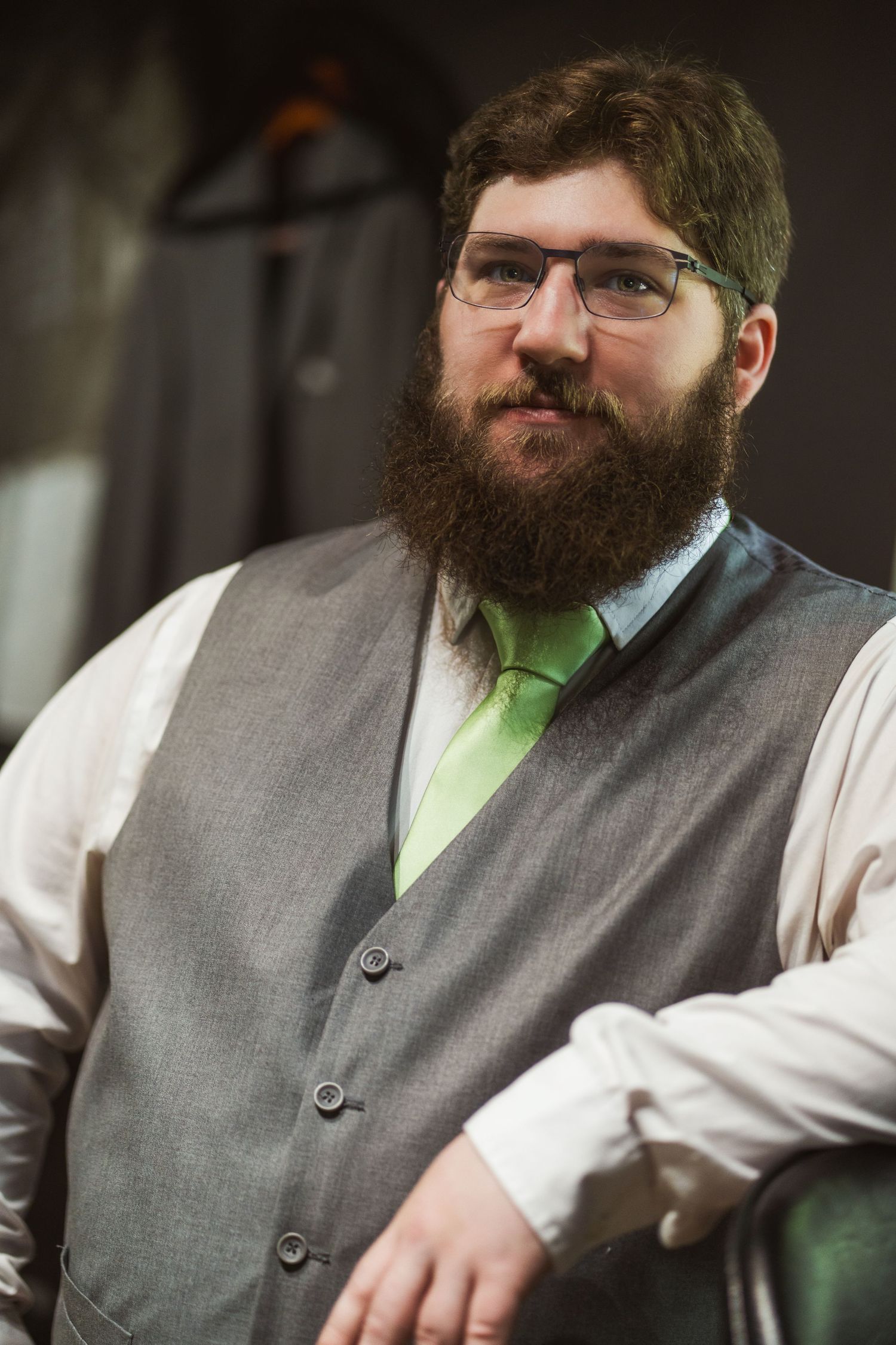 A bearded man in glasses wearing a grey vest and lime green tie sits in contemplative poses across multiple frames.
