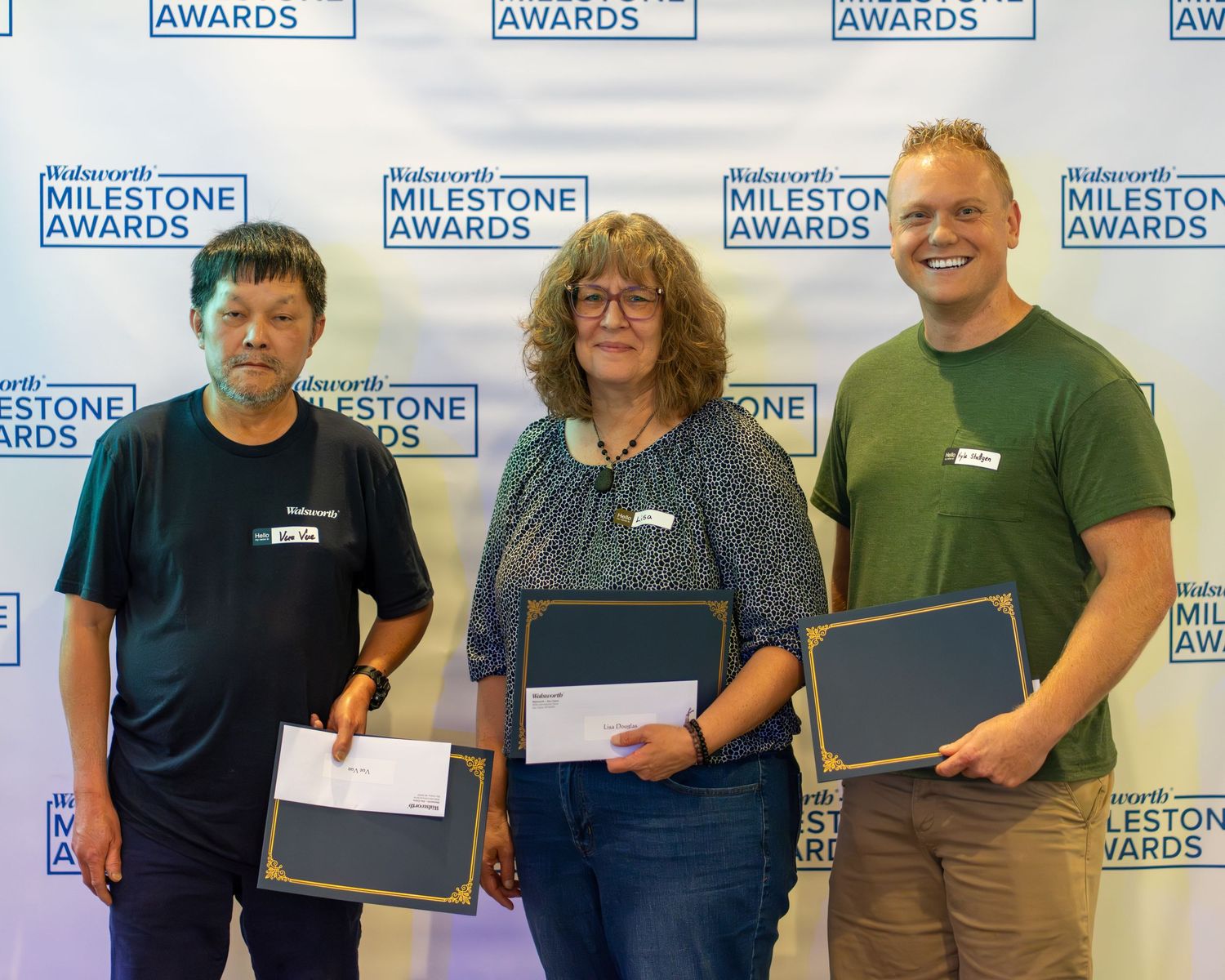 A group of people standing in a row holding certificates at an awards ceremony with a branded backdrop.