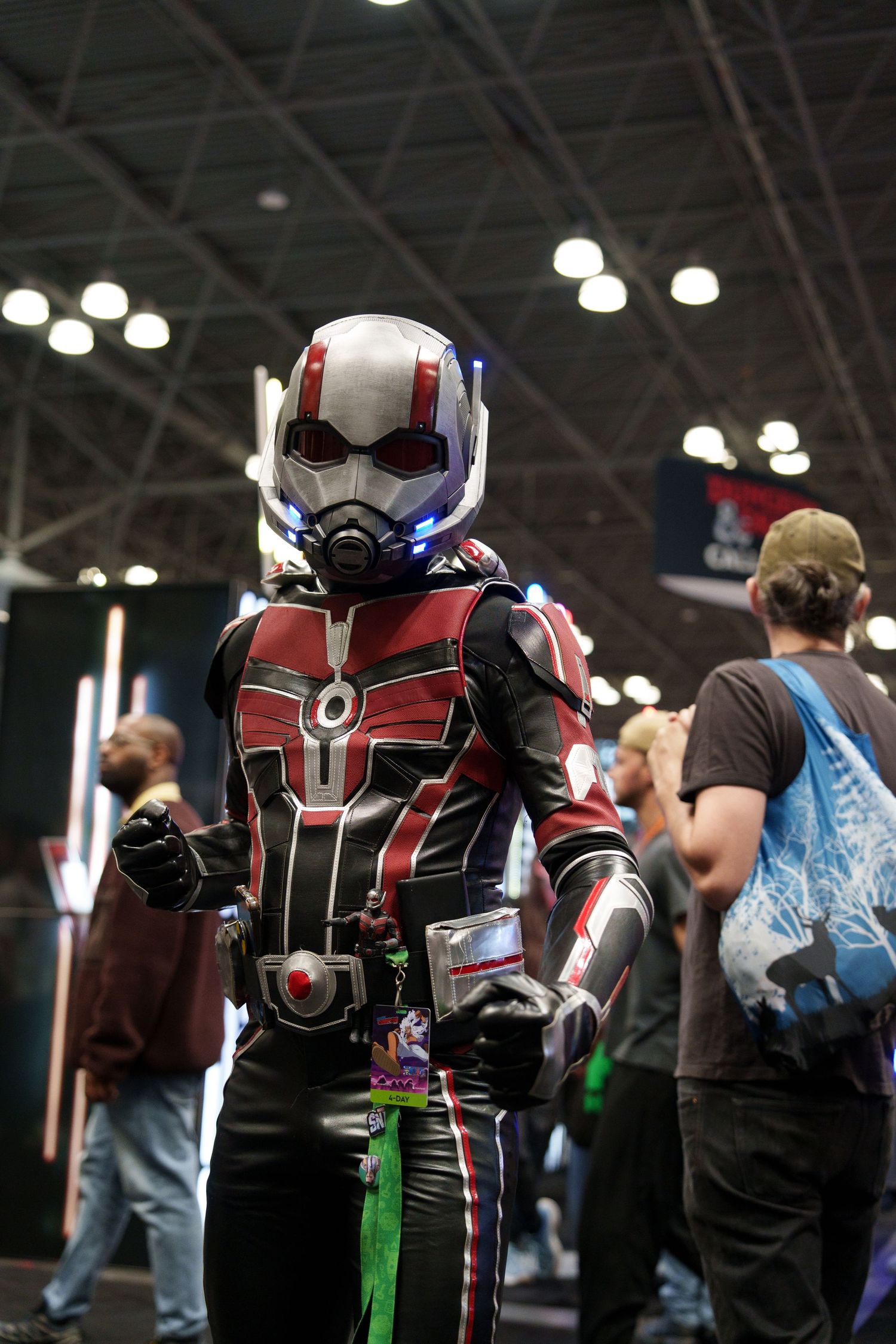 Person in detailed Ant-Man cosplay suit at a comic convention, wearing red and black armor with helmet.