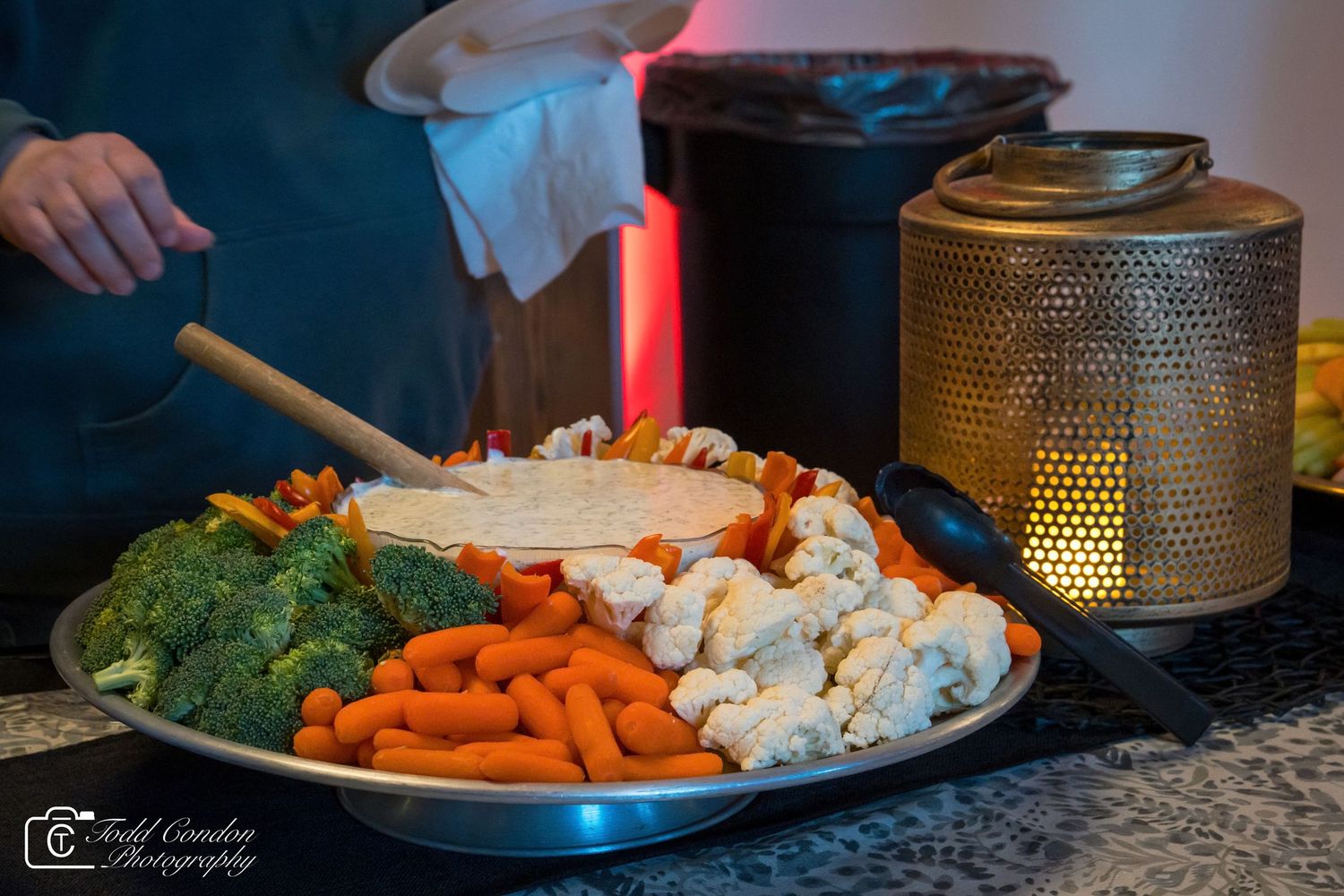 A colorful vegetable platter with carrots, broccoli, cauliflower, and dip served at a catered event.