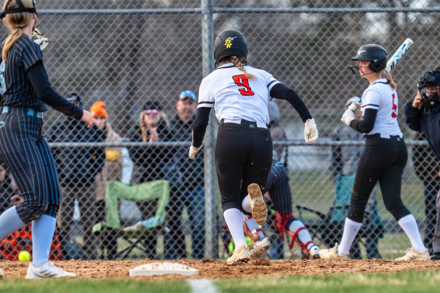 Baseball player slides into base during intense game action as fielder attempts to make the tag.