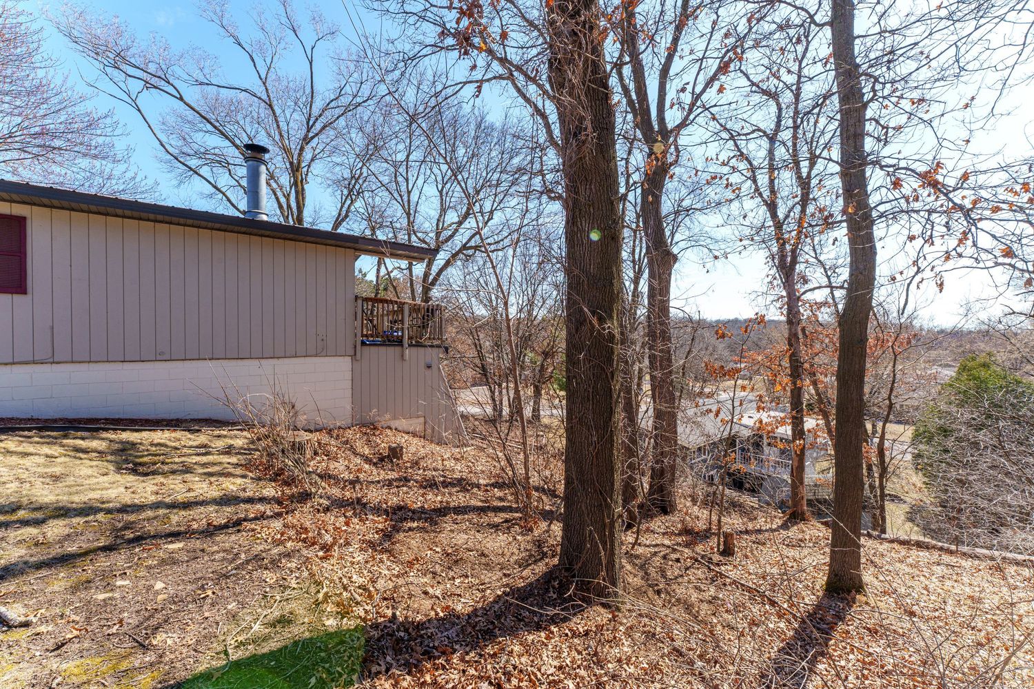 Exterior view of residential buildings on a wooded lot with fallen leaves.