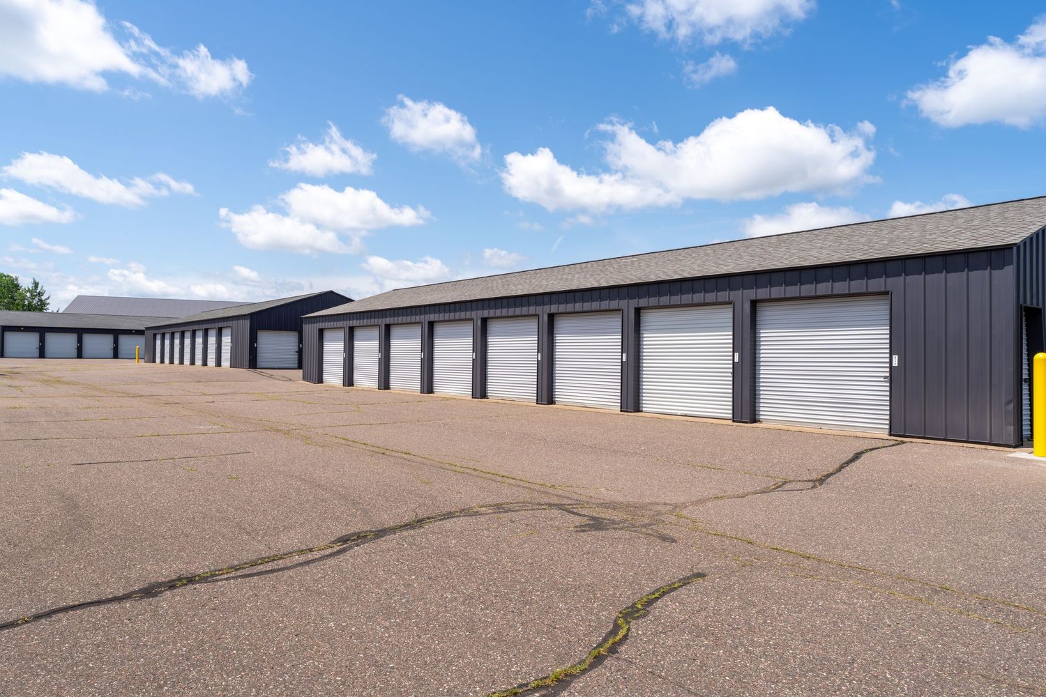 A panoramic view of modern storage units with brown gravel driveways under a bright blue sky with white clouds.