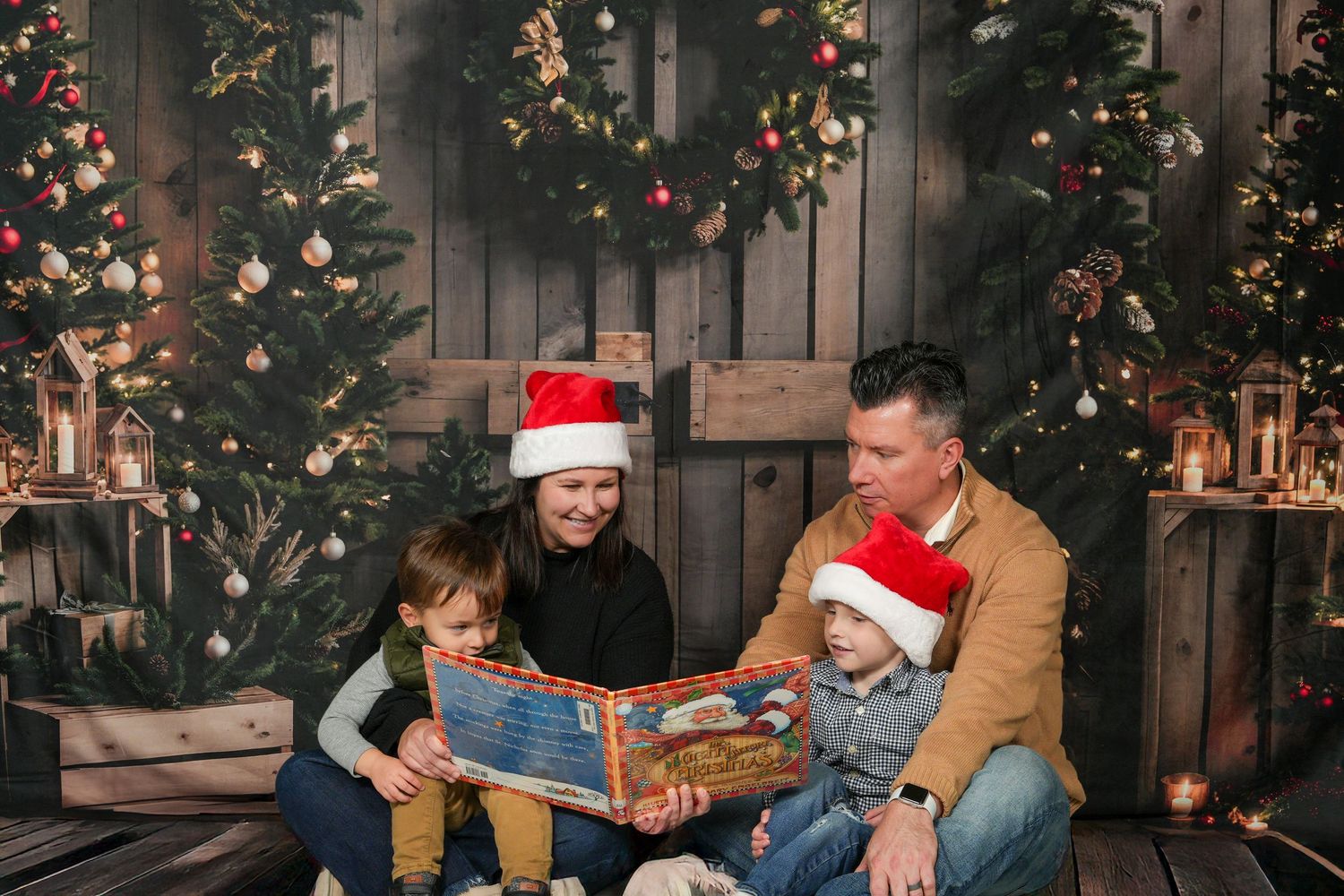 Two people in holiday attire exchange Christmas gifts while sitting on a couch in front of a decorated tree.