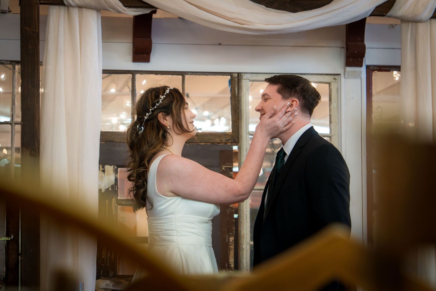A couple shares their first dance at a wedding reception under elegant white fabric draping and soft lighting.