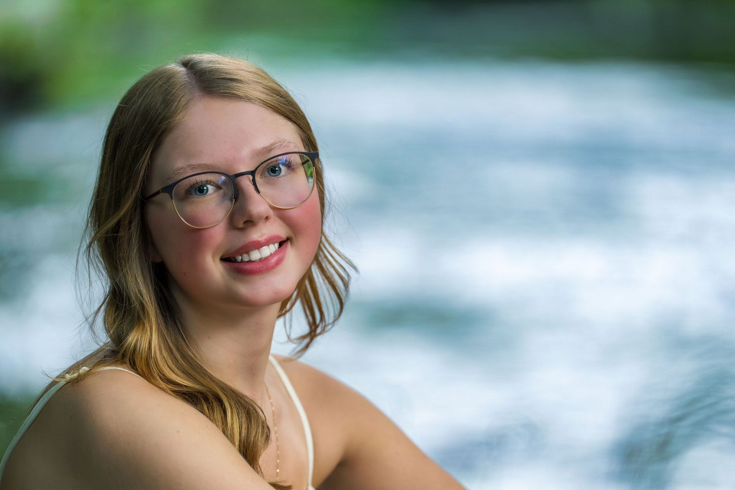 Portrait session by a rushing river with sunlit water and natural greenery in the background.