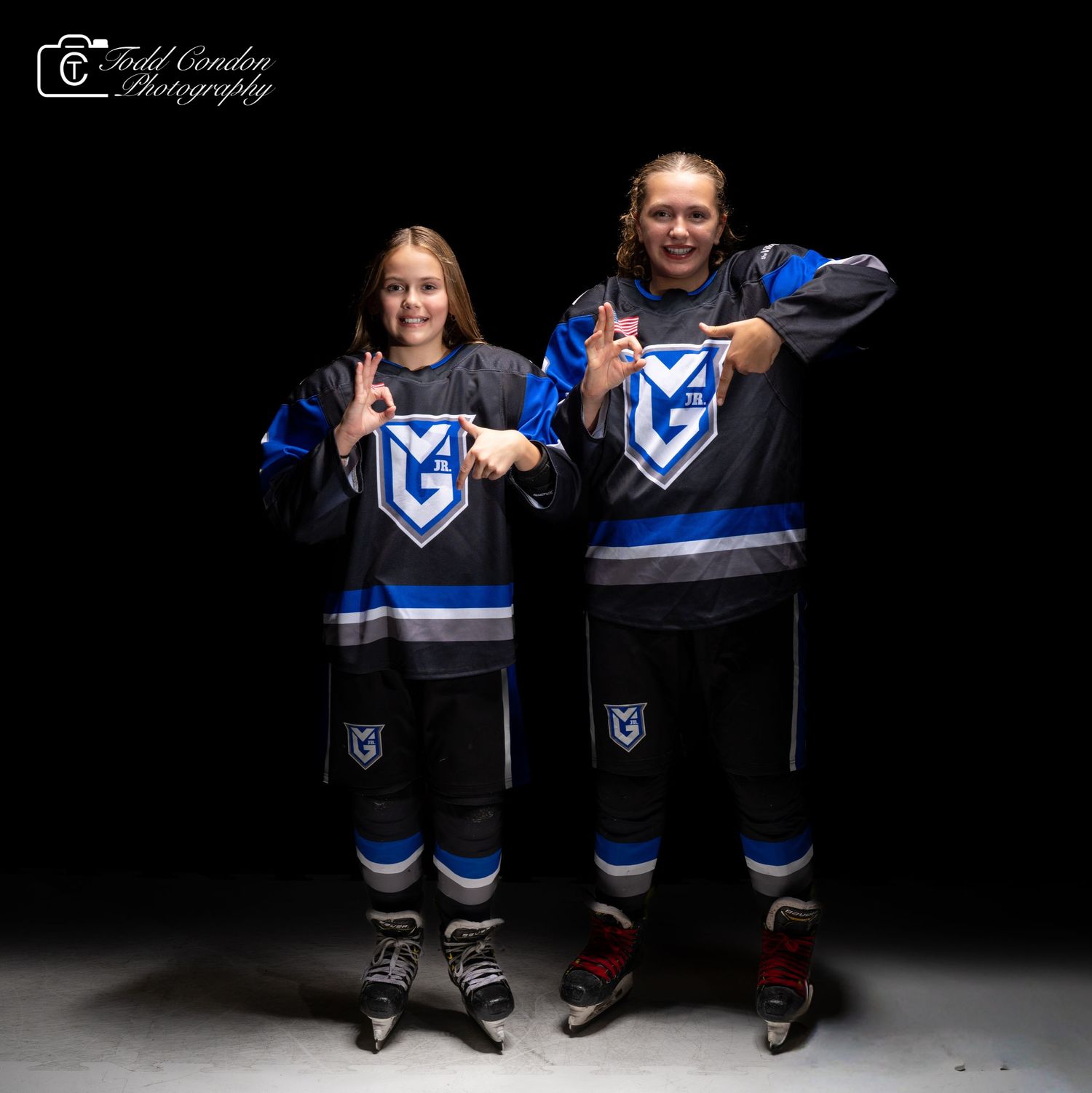 Two people wearing matching blue and white hockey jerseys pose together against a dark background.