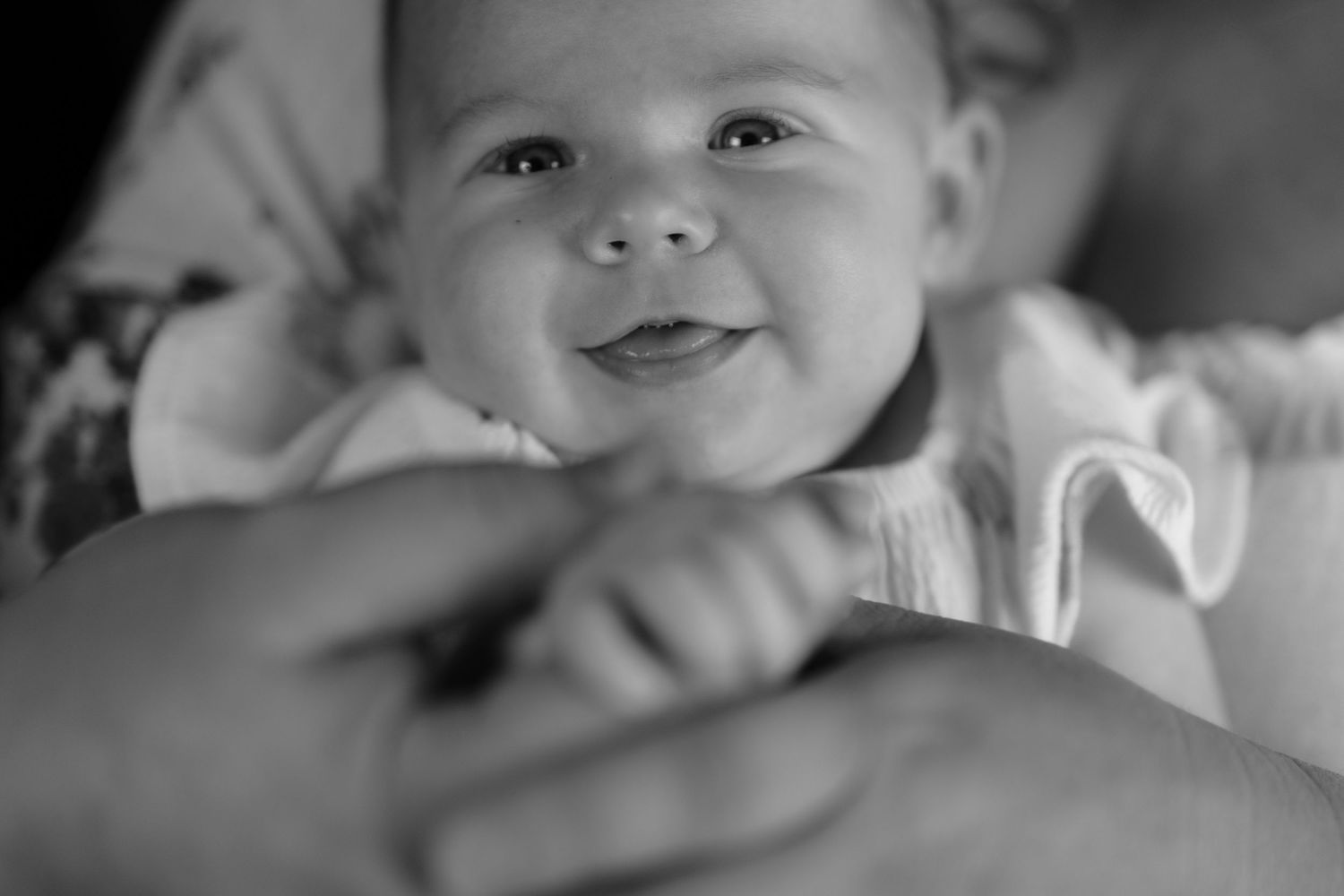 Black and white photo of a smiling baby being held by an adult, capturing a joyful and tender moment.