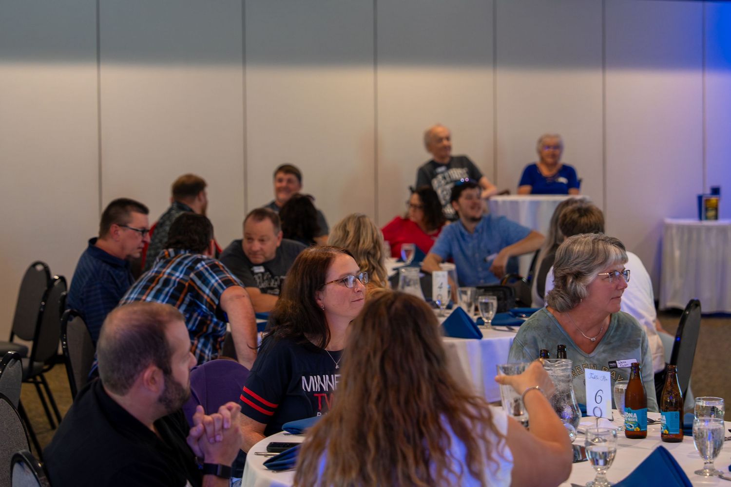 People sitting at round tables in a conference room with blue lighting during a professional event.