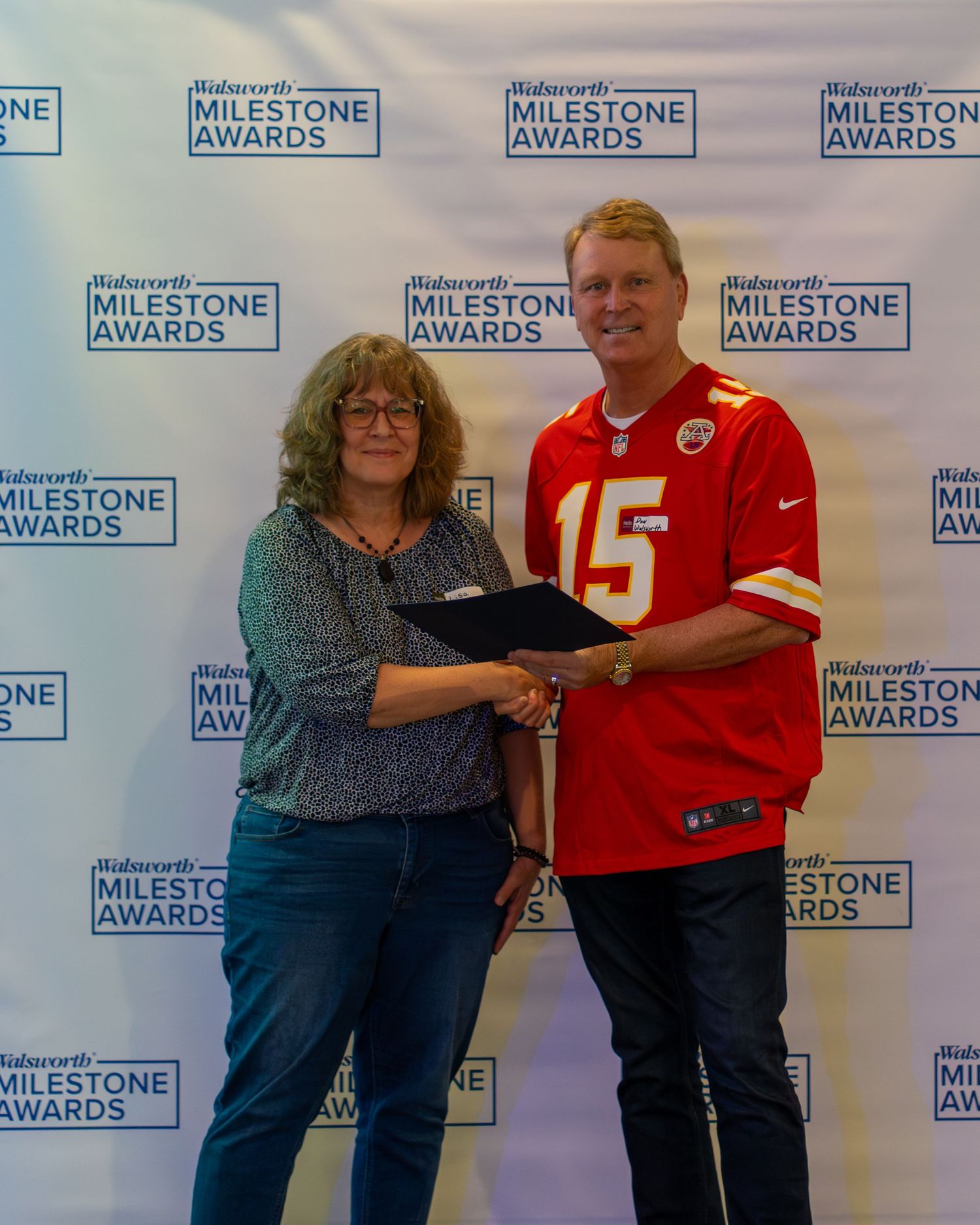 People in red sports jerseys and casual attire pose together against a branded backdrop with Milestone Awards logos.