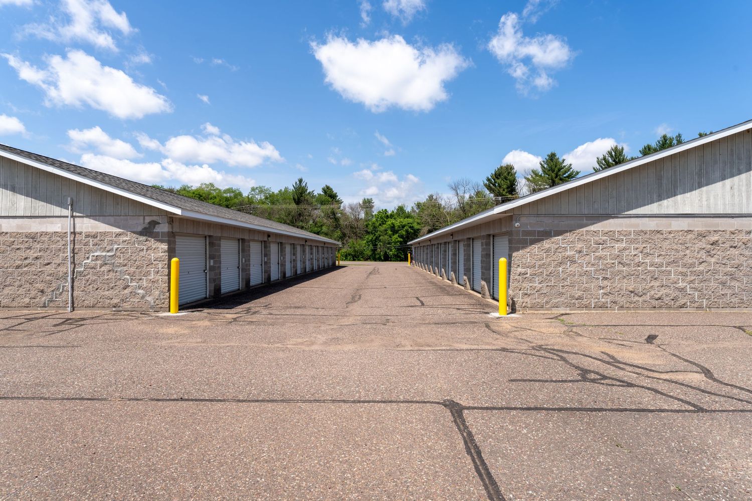 Panoramic view of self storage units with beige walls and yellow doors under a bright blue sky with white clouds.