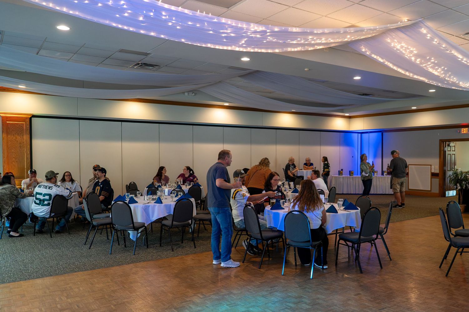 A large banquet hall with string lights on the ceiling and people seated at round tables during an event.