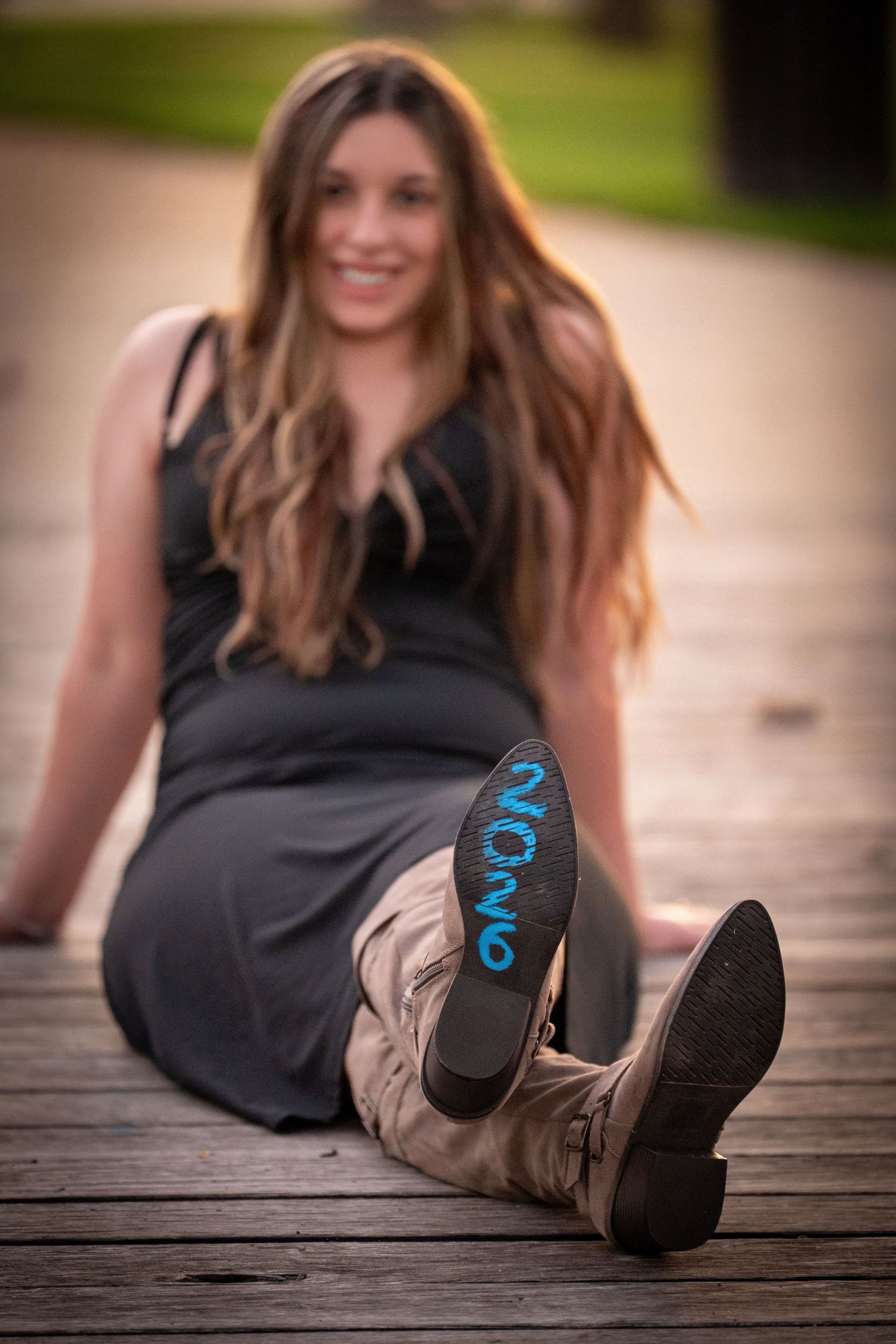 A person in a black dress lies on a wooden deck while wearing tan boots with blue numbers written on the soles.
