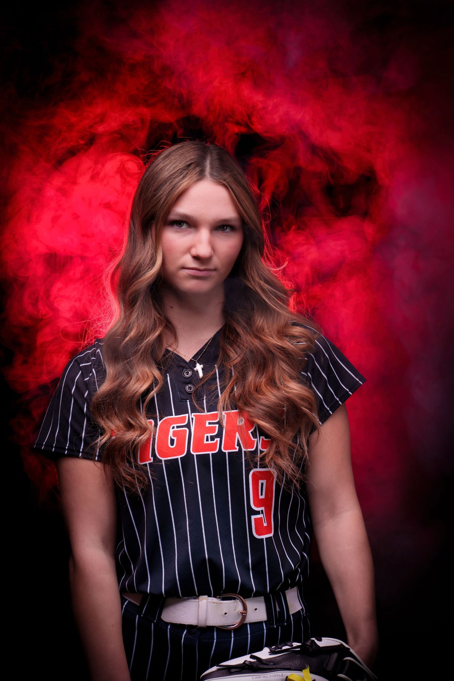 Female softball player #9 in Tigers pinstripe uniform poses dramatically against a dark background with red smoke.