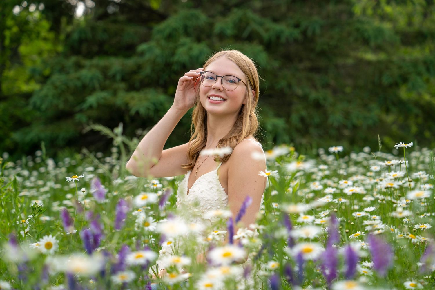 A person in a floral dress lies among blooming daisies and wildflowers in a sunny meadow.