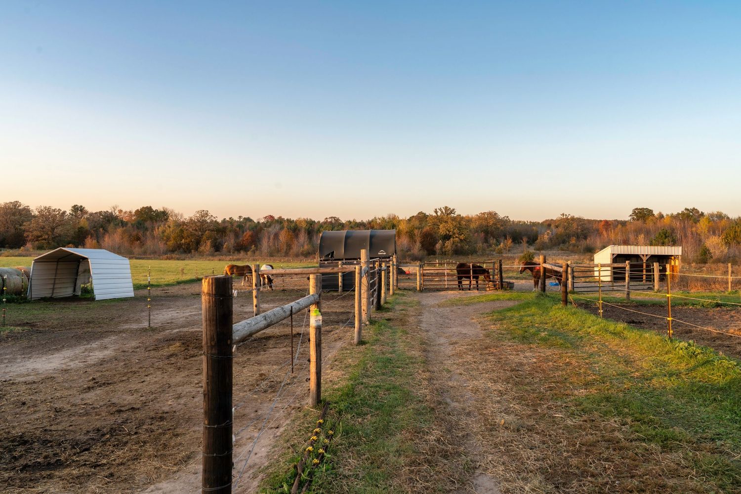 Horse riding arena at sunset with wooden fence posts and dirt ground.