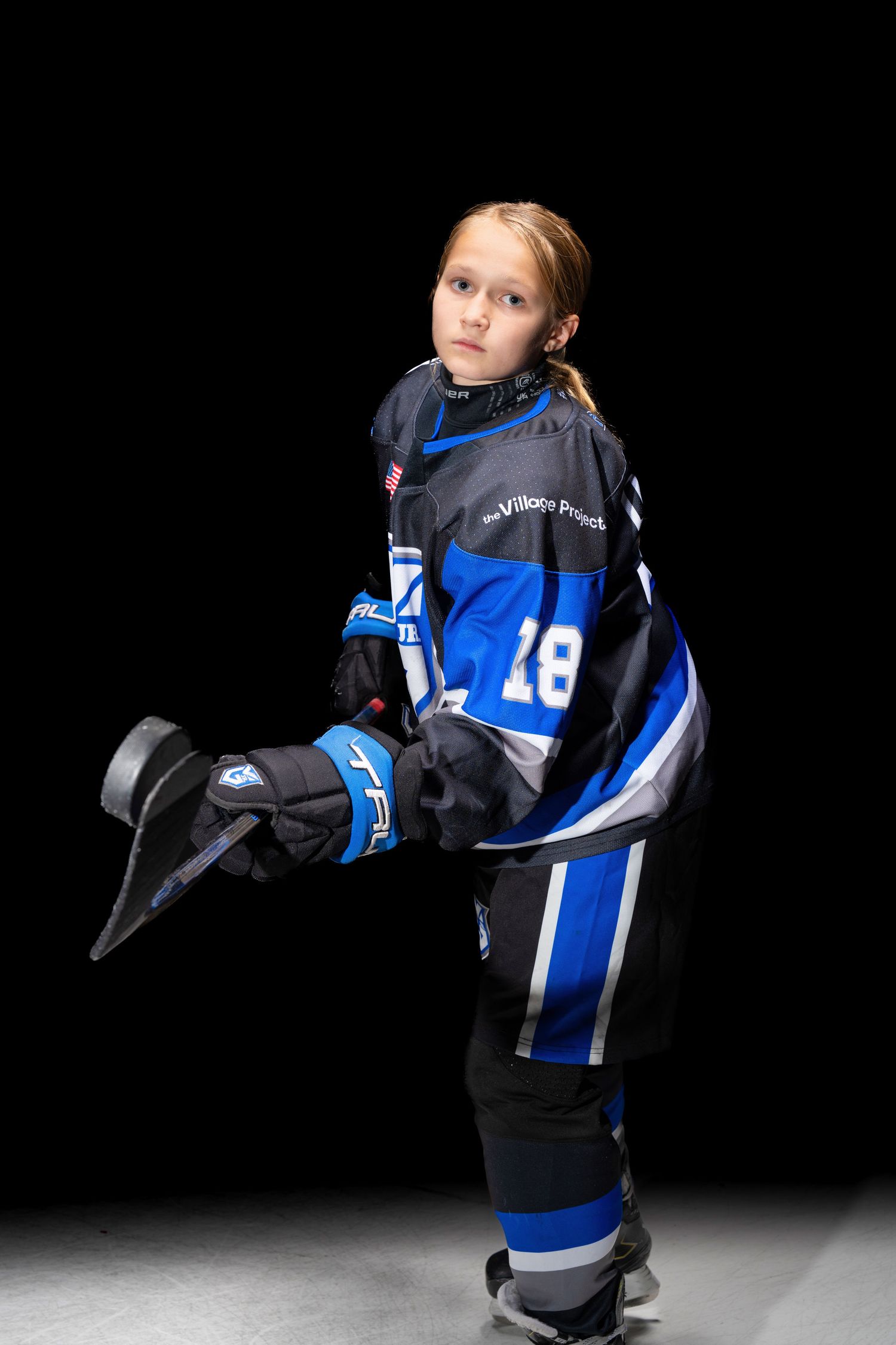 Young hockey player in blue and black jersey number 28 poses in full gear against dark background.