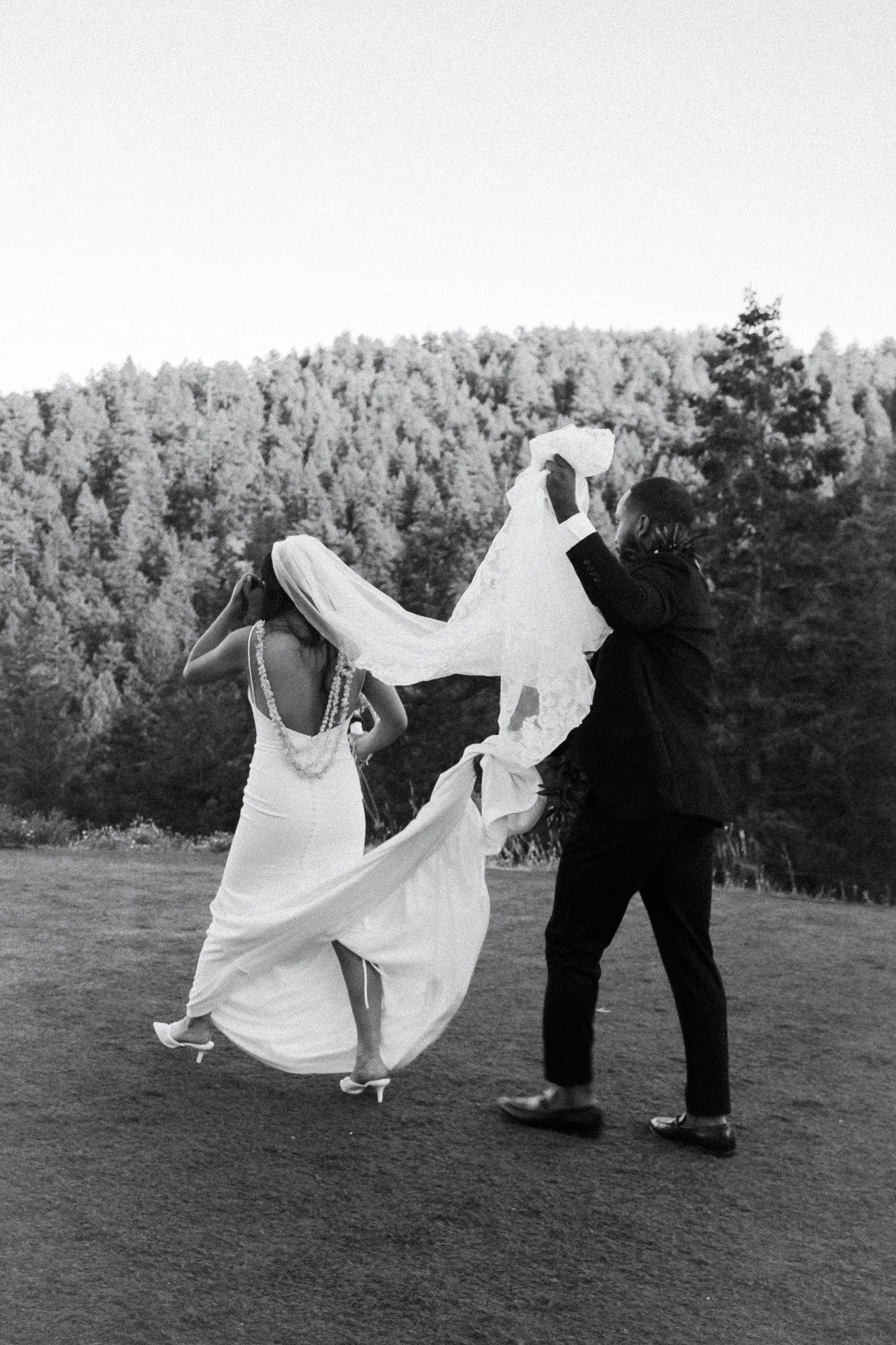Groom helping bride carry her dress through a field in Colorado.