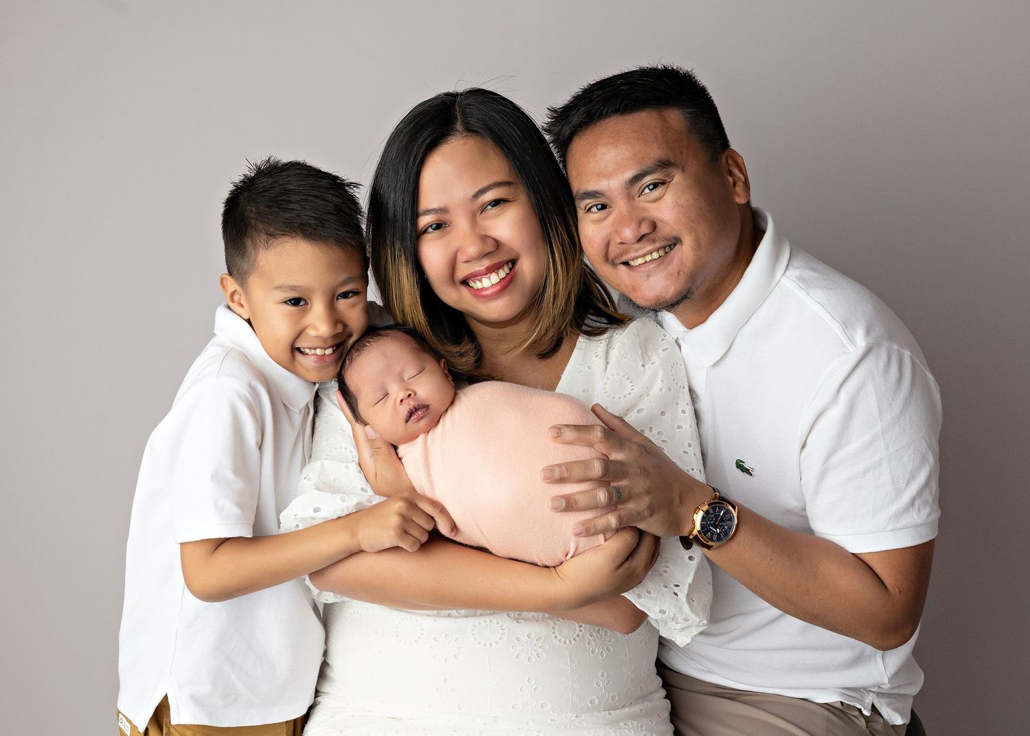 A series of maternity photos showing a family in white clothing posing together with a pregnant belly against a gray backdrop.