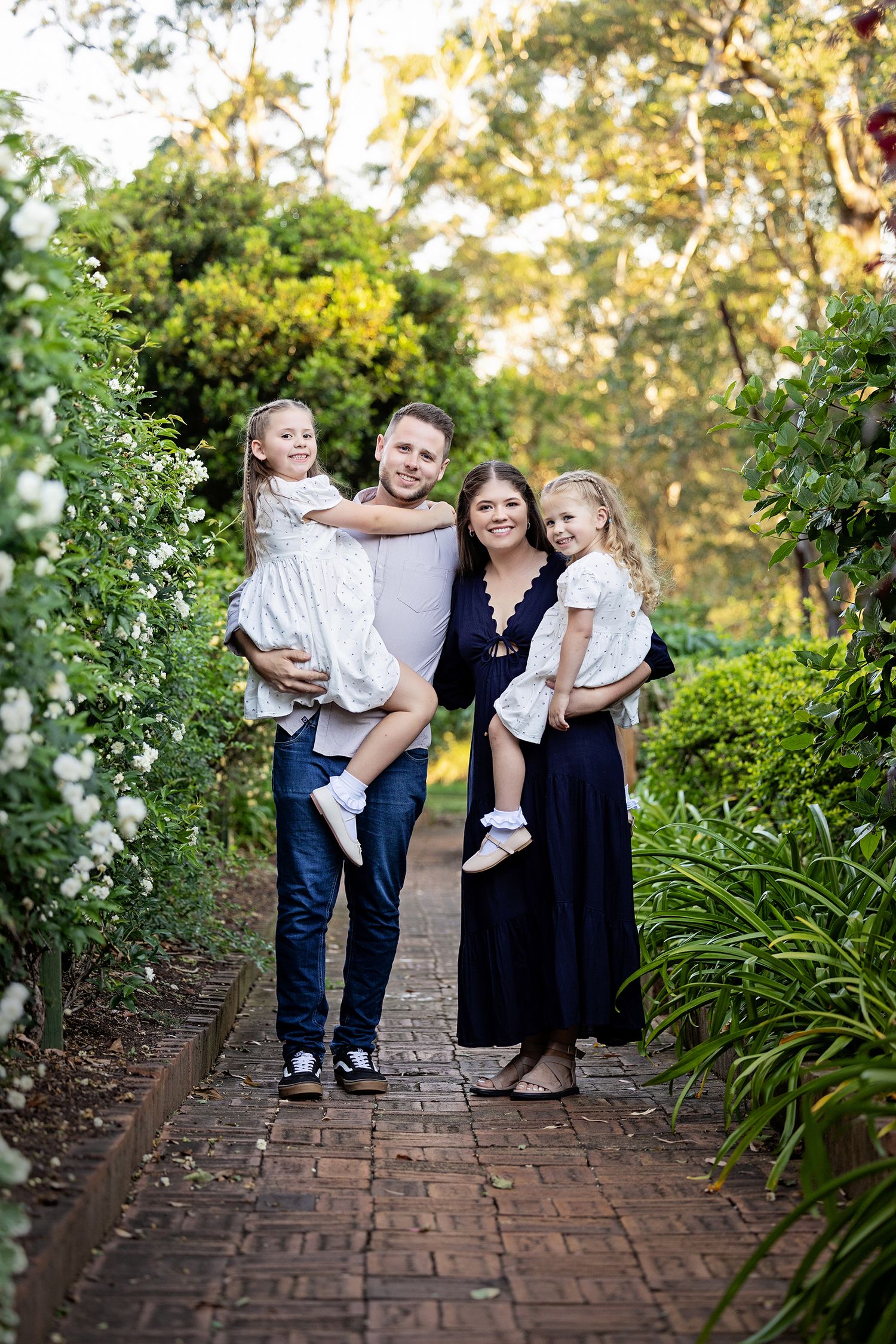 A family portrait on a garden path lined with blooming flowers and greeneryToowoomba Photographer Toowoomba Newborn Photographer