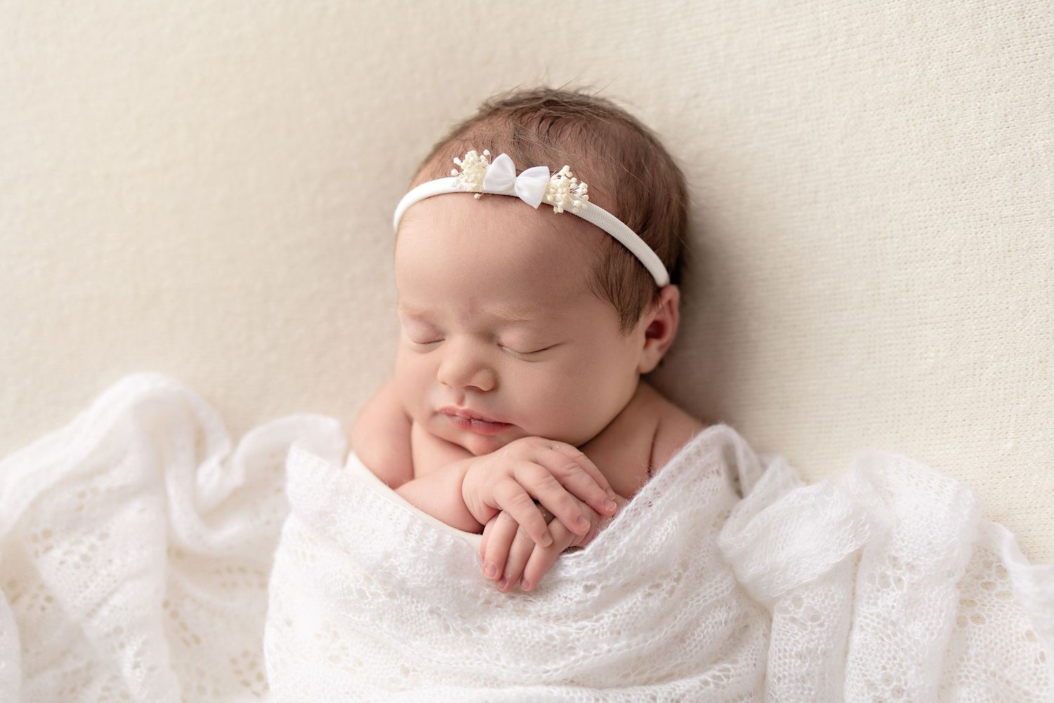 Peaceful sleeping newborn baby girl wrapped in white lace, wearing a delicate floral headband.