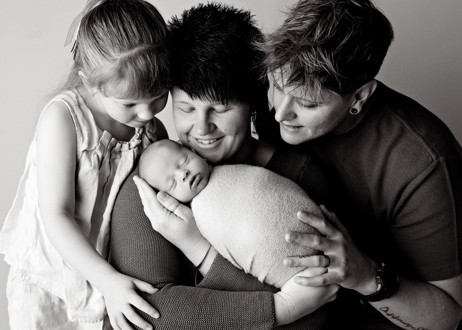 Black and white family portrait of two women with a young girl and sleeping newborn baby.