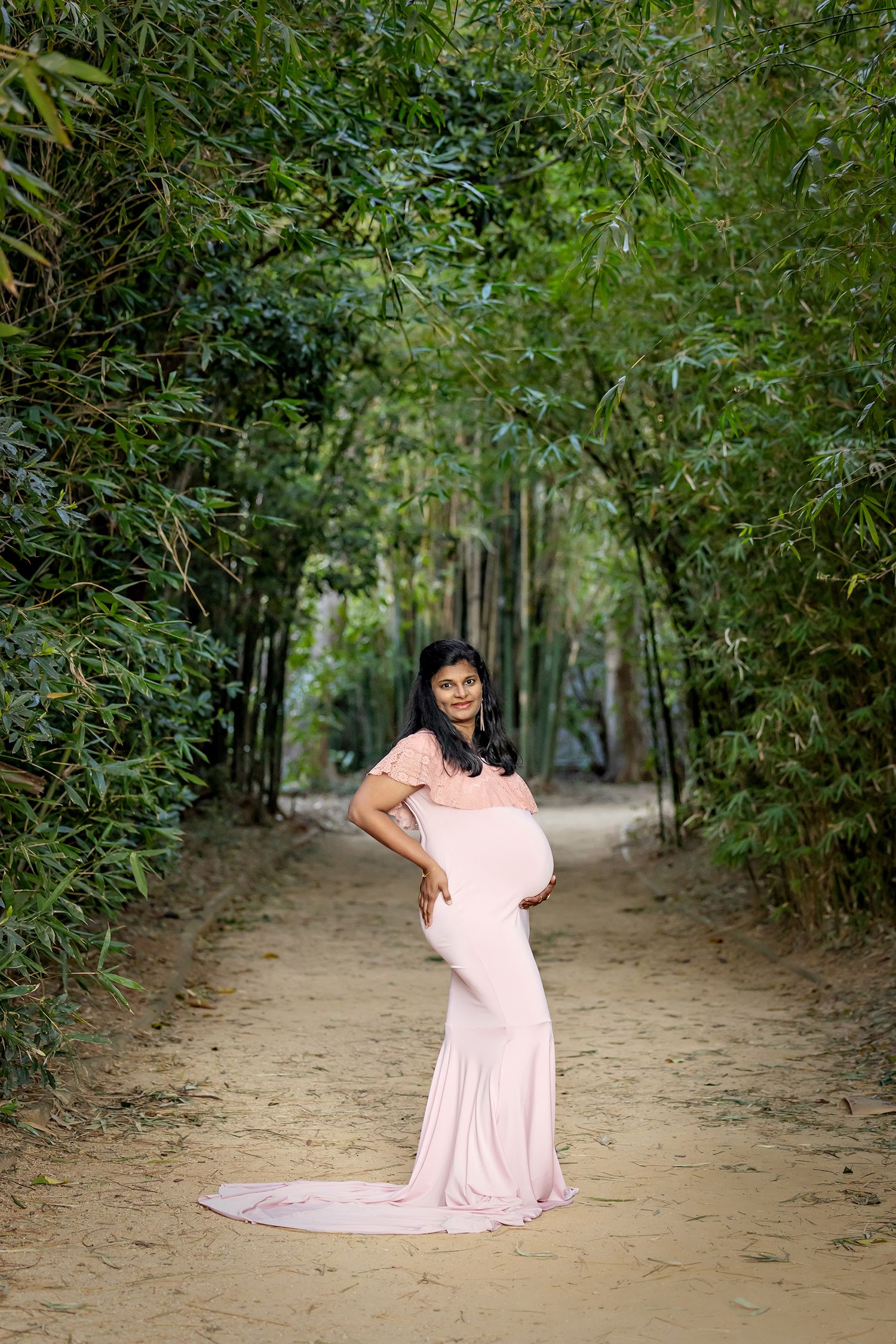 A pink flowy dress stands out against a natural wooded path backdrop.