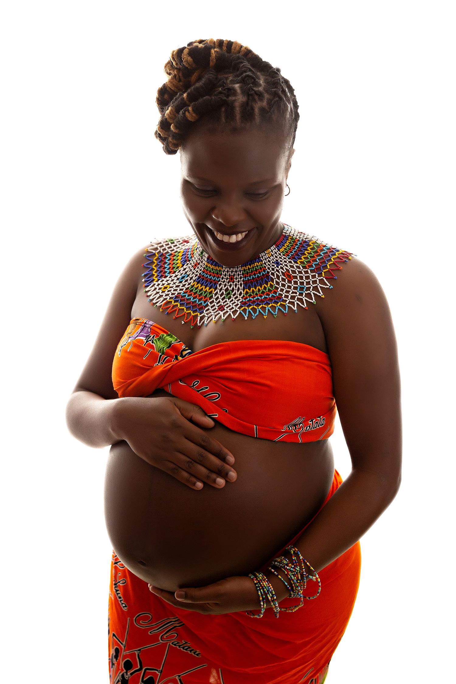 Expectant mother in traditional African attire and beaded necklace smiling while holding belly.