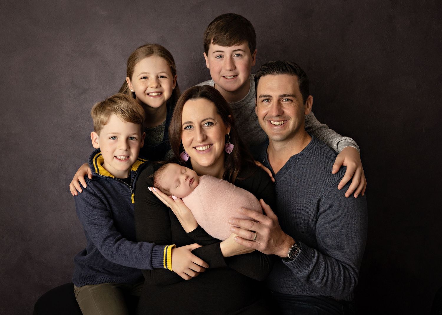 A loving family portrait series showing warm embraces and candid moments against a dark studio backdrop.
