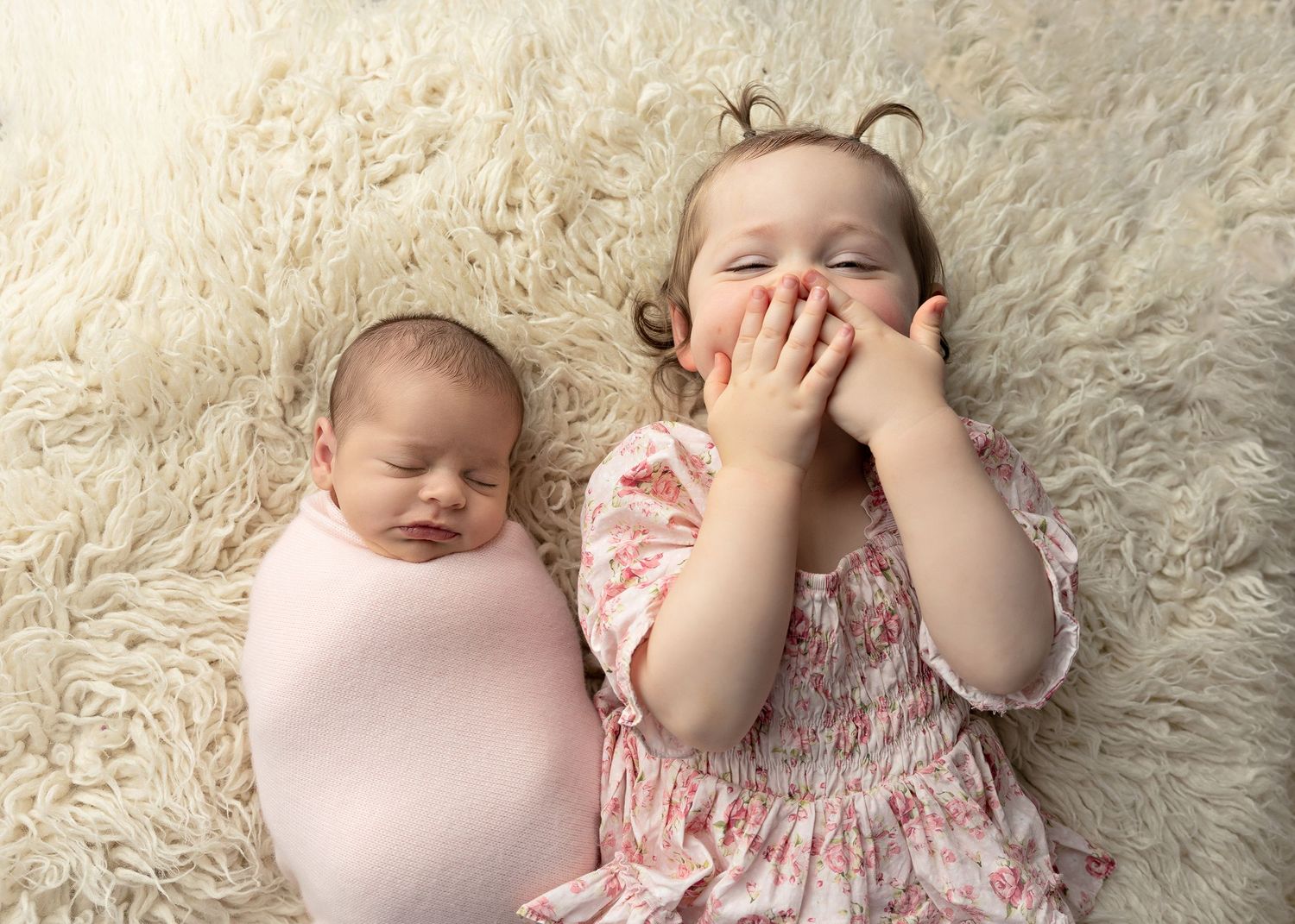 Siblings laying on plush white carpet wearing soft pink and floral outfits. Toowoomba Photographer