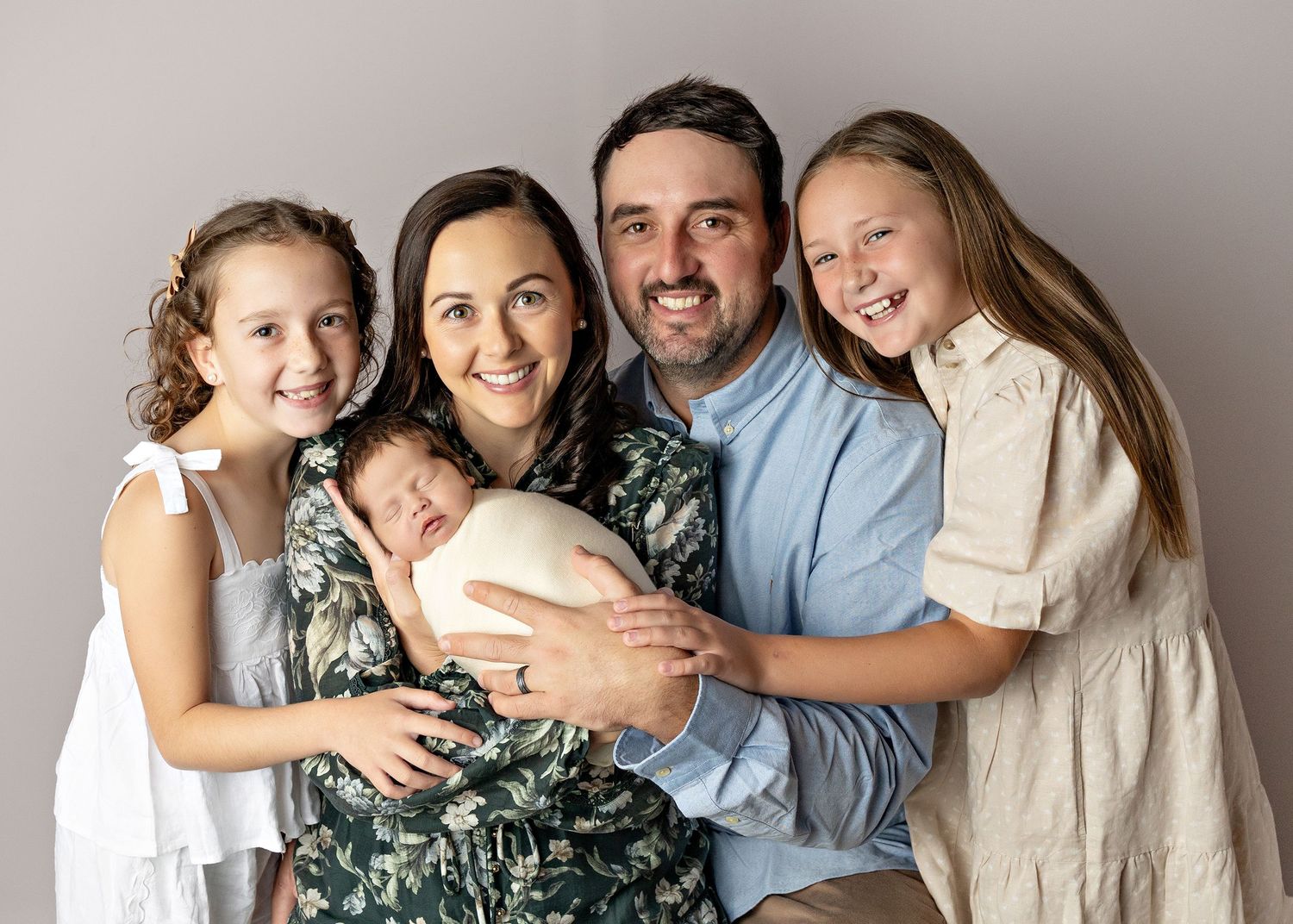 A family wearing coordinated outfits in green and white poses together against a neutral backdrop for portraits.