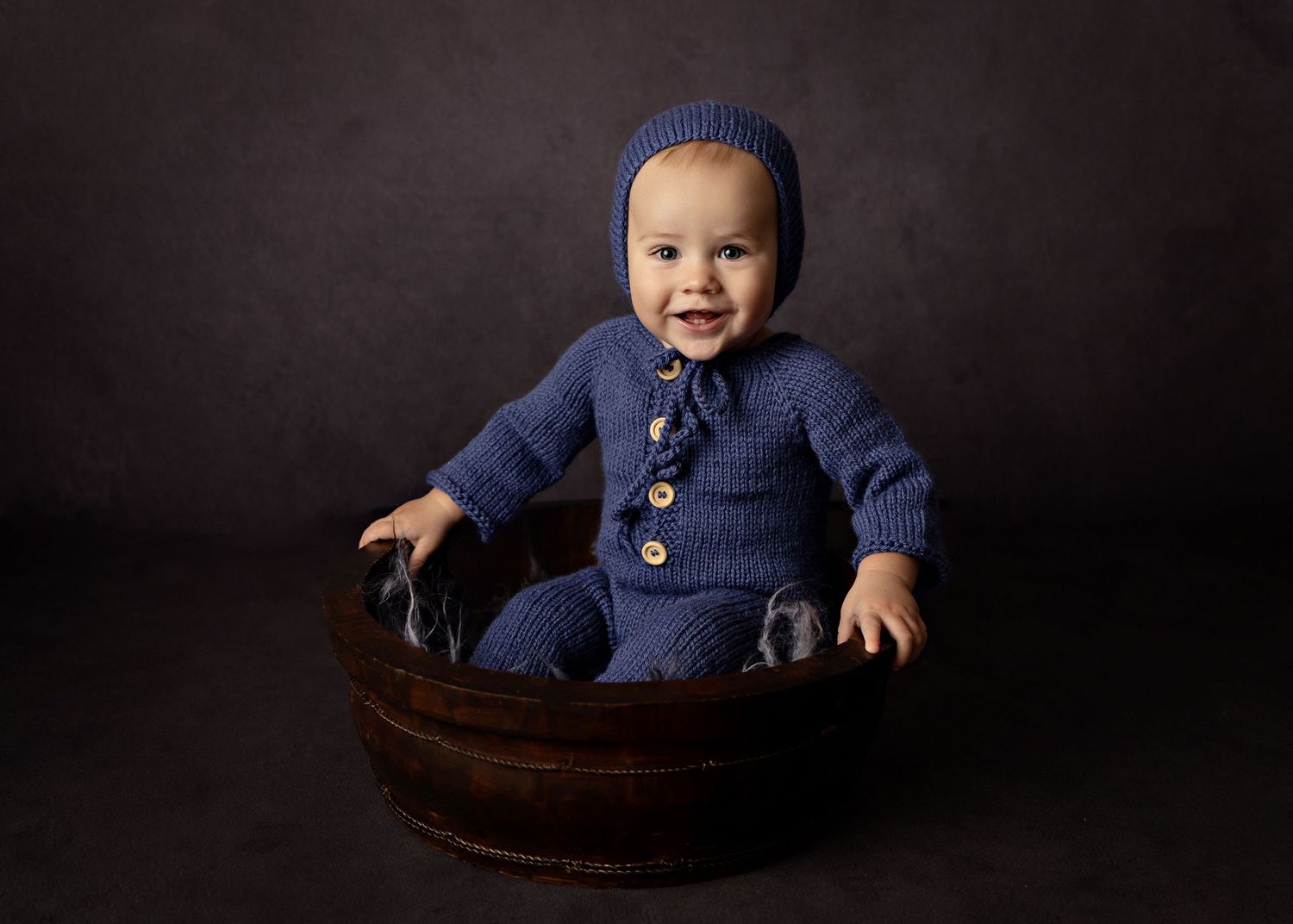 Baby wearing navy blue outfit sitting in wooden bowl against dark backgroundToowoomba Photographer Toowoomba Newborn Photographer