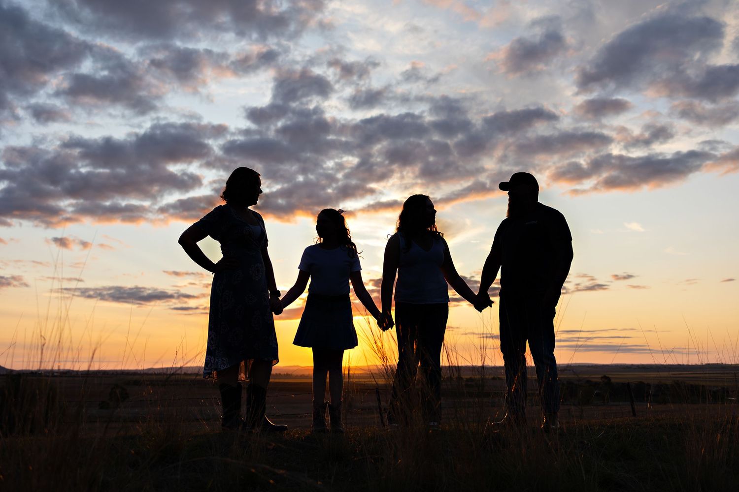 Silhouettes of a family holding hands against a dramatic sunset skyToowoomba Photographer Toowoomba Newborn Photographer