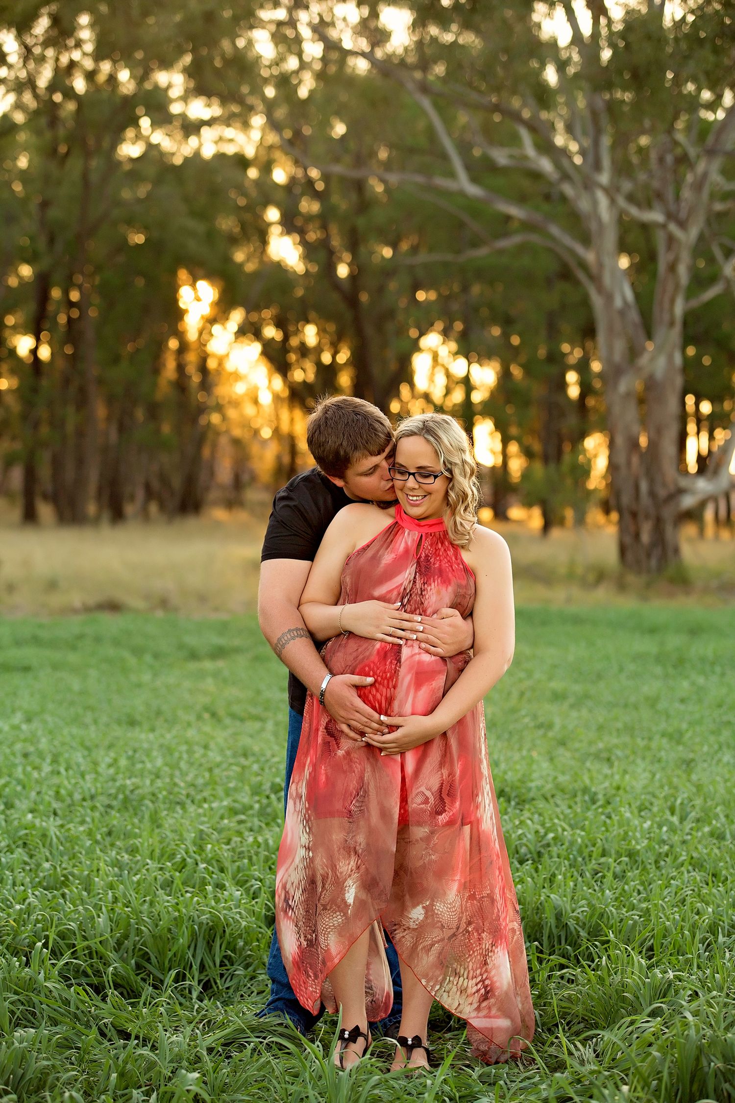 Romantic portraits in a green field with sunset light filtering through trees.