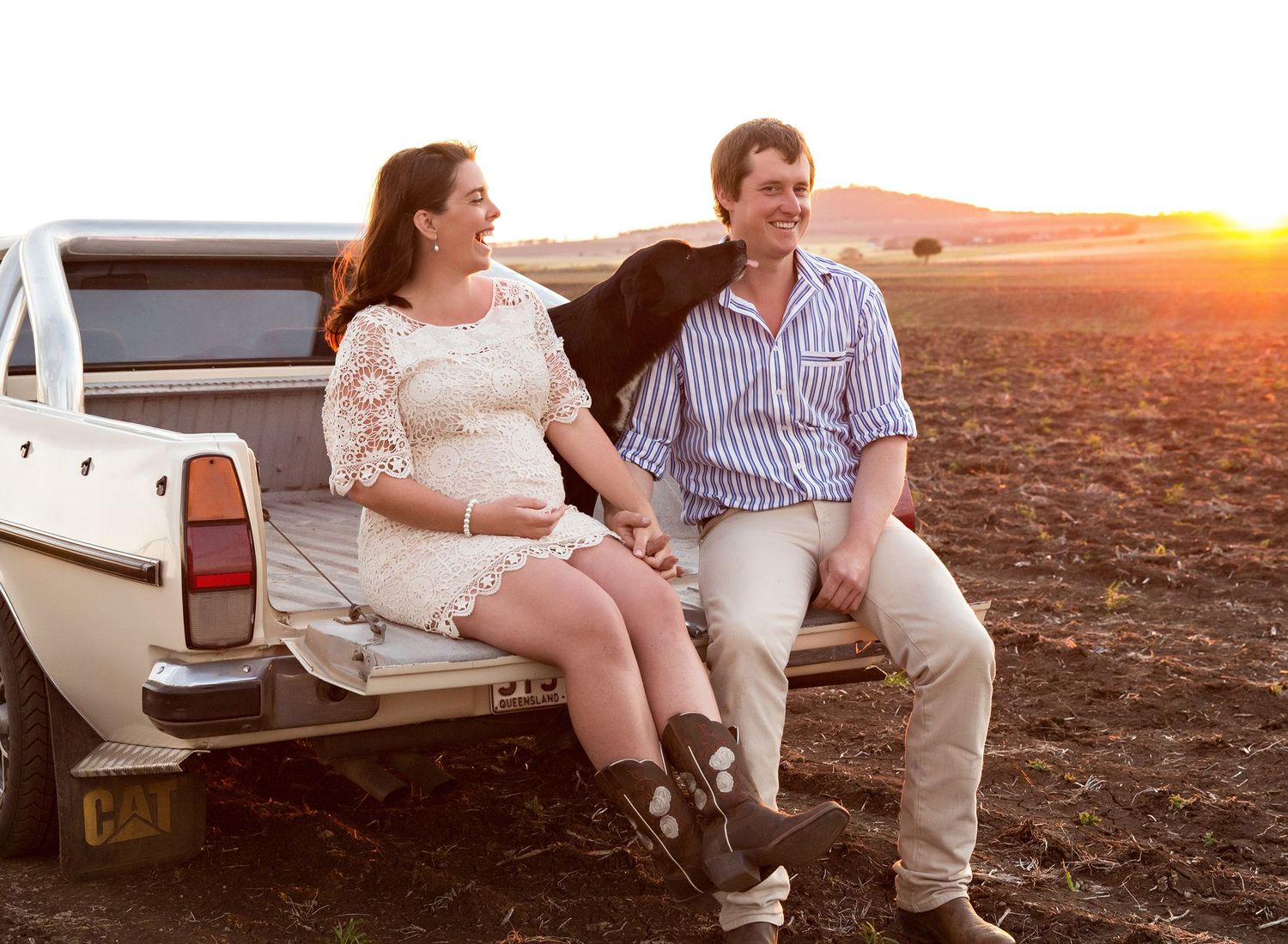 Couple sits together on tailgate of vintage pickup truck at sunset.