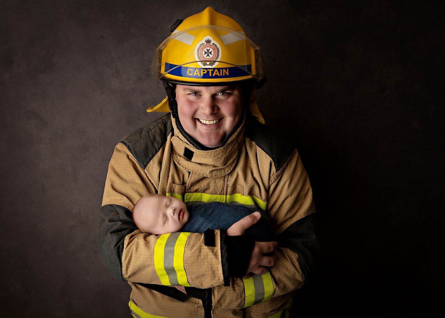 A firefighter in protective gear and yellow helmet stands against a dark background.